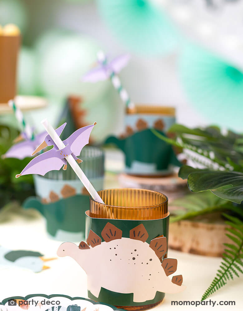 A dinosaur themed birthday party table featuring Momo Party's dinosaur cup sleeves and Pterodactyl paper straws, with tropical themed plants around the table, making this a great inspo for a modern and stylish kid's dinosaur themed party.