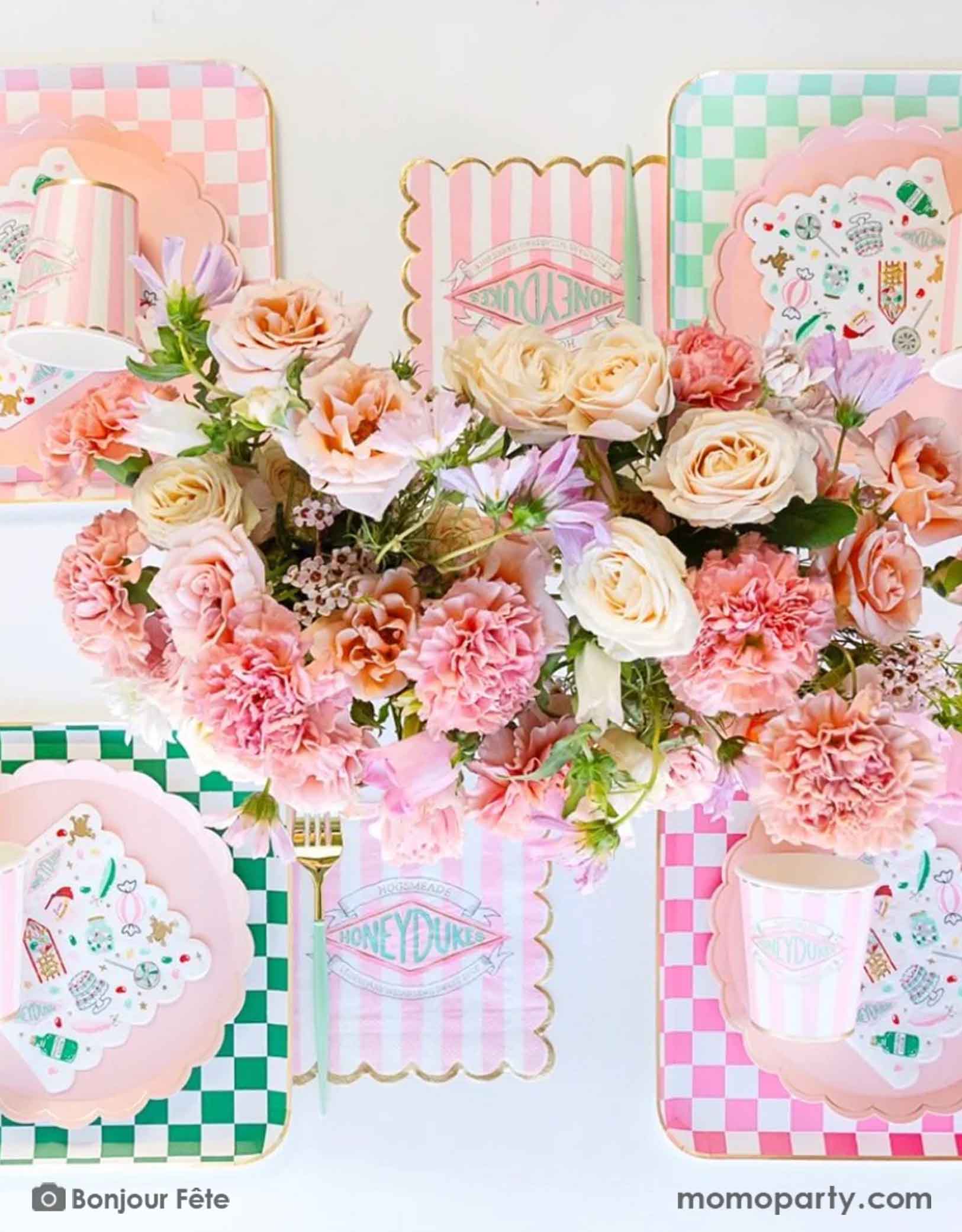 A modern and beautiful table setting featuring Harry Potter Honeydukes themed party supplies in pink and green including pink and green checkered dinner plates, pink striped Honeyduke large napkins, party cups and matching napkins. With a beautiful floral bouquet in the middle, this makes a modern and elegant party table setting for kid's girly Harry Potter themed birthday celebration.