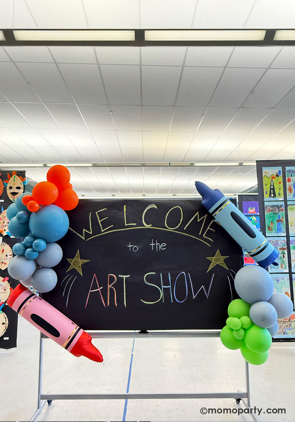 A school chalkboard decorated with a festive and colorful balloon garland along with Momo Party's 40" x 9" blue & red crayon shaped foil balloons at a kid's art show in a school event. This easy balloon installation with bright color and fun design is also perfect for kid's school themed celebration, be it a back to school party, a first day of school celebration or any kids event at school.