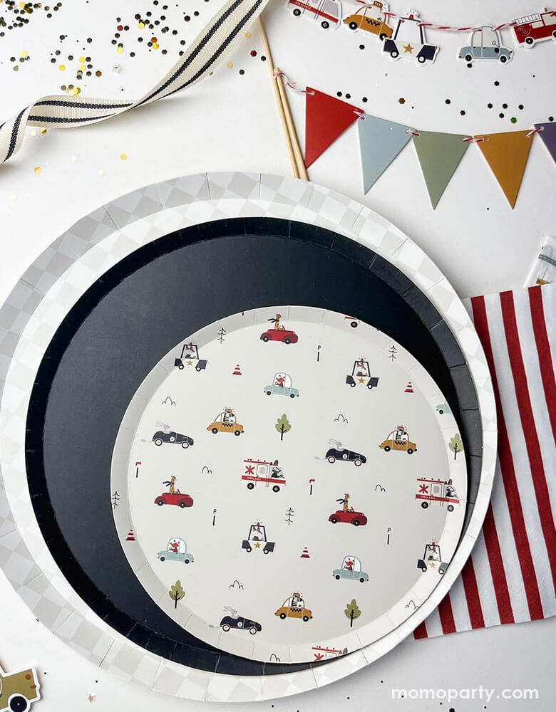 A festive kid's vehicle themed party tablescape featuring Momo Party's 10.25" light grey checkered dinner plate, 9" navy large plate and a round side paper plate with multiple colorful vehicle illustrations on it including ambulance trucks, police cars, taxi cars, and cars by Josi James. Around the party plates are red striped paper napkins, birthday cake pennant flag and vehicle cake toppers, along with ribbons and confetti, this makes a great inspiration for a preschool boy's birthday party decoration!