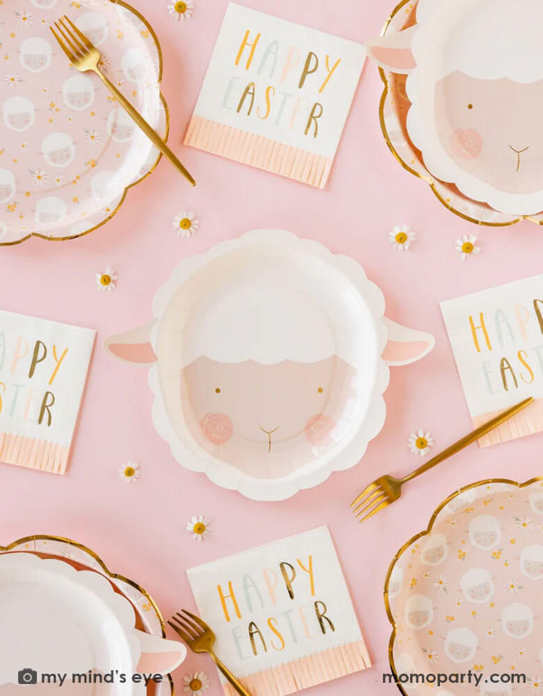 A table-setting featuring Momo Party's 9" x 9" lamb head shaped plates in adorable water color design by My Mind's Eye. Around the plates are pink scatter lamb scalloped plates and Happy Easter pink fringe napkins. With daisy flower confetti and gold forks, it creates a darling vibe for a kid's friendly Easter tablescape.