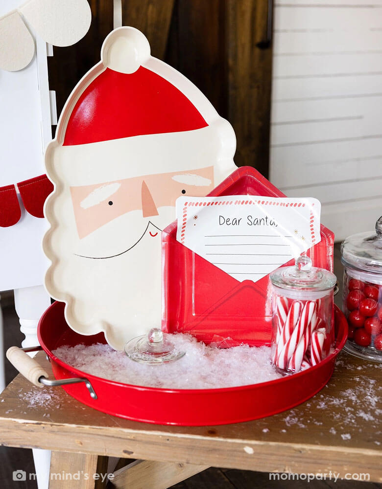 A hot cocoa station set up ideas in a kid's Holiday party featuring Momo Party's Letter to Santa envelope shaped plate, Santa shaped bamboo tray along with jars of candy canes, red gum balls in a red round tin tray. With the artificial snow decoration around, this make s a whimsical decoration for a festive Christmas celebration!