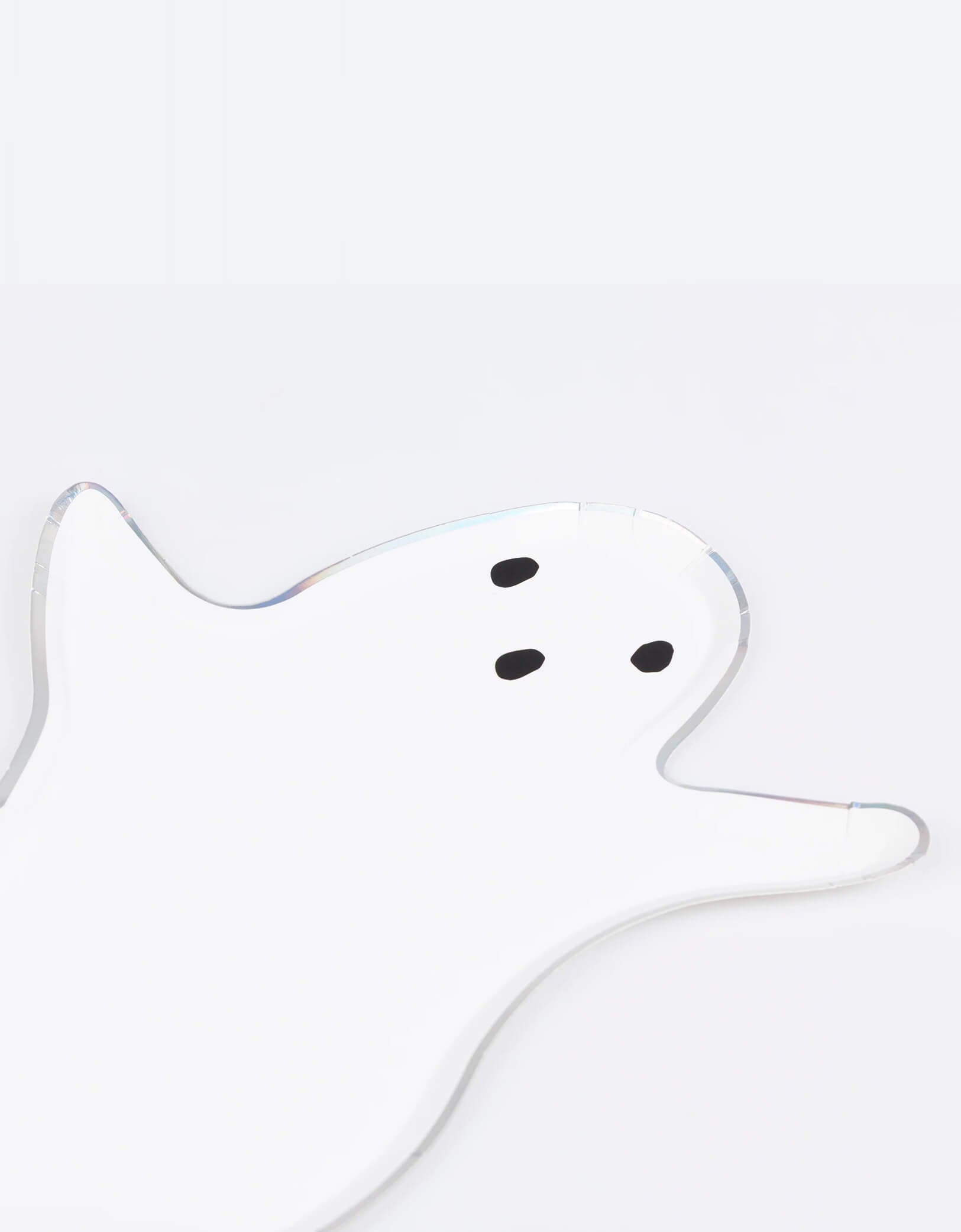 A close up of Momo Party's 9" x 13.25" ghost shaped plate by Meri Meri on a white background. Designed with a classic floaty ghost silhouette and a dazzling silver holographic foil border, they create a hauntingly cool effect. Perfect for kid-friendly gatherings or creepy cocktail parties!