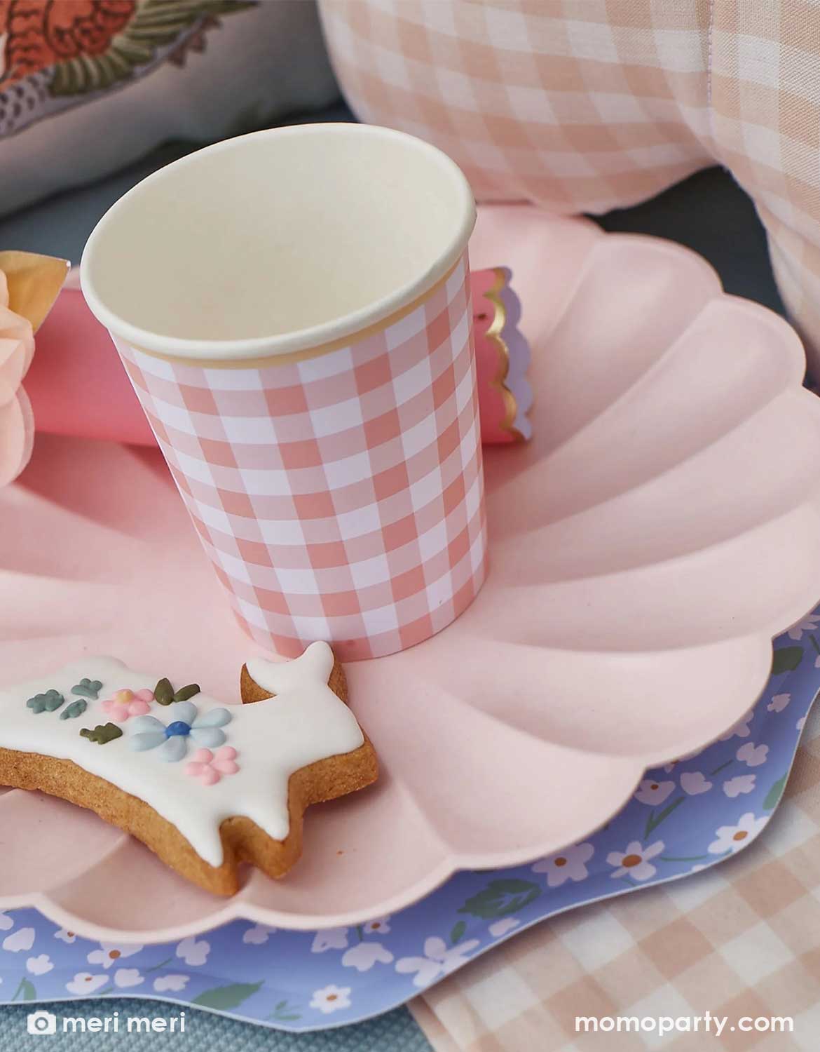 Momo Party's pink gingham checkered paper cup on a ditsy flower decorative plate with a bunny shaped cookie, on a checkered tablecloth. A perfect inspo for a spring inspired party or an Easter celebration.