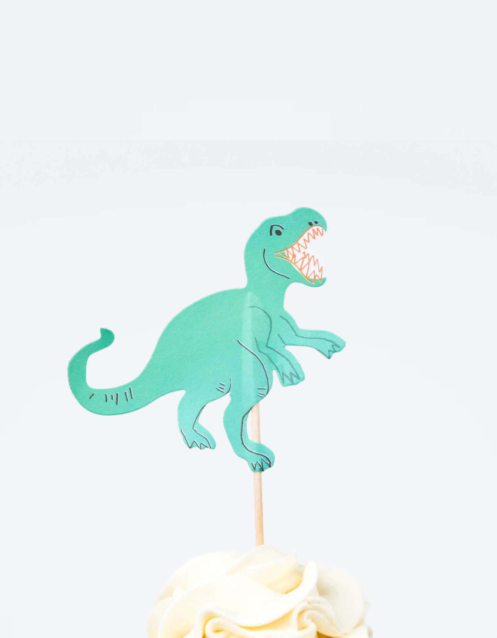 A cupcake decorated with Momo Party's T-rex cupcake topper by Meri Meri. This fun kit also makes a great gift for kids who love to bake.