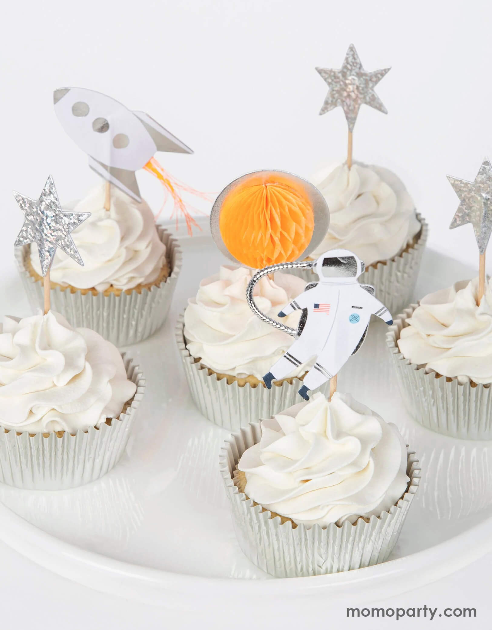 Cupcakes with space-themed toppers including a rocket, moon, and astronaut from Momo Party on a white background.