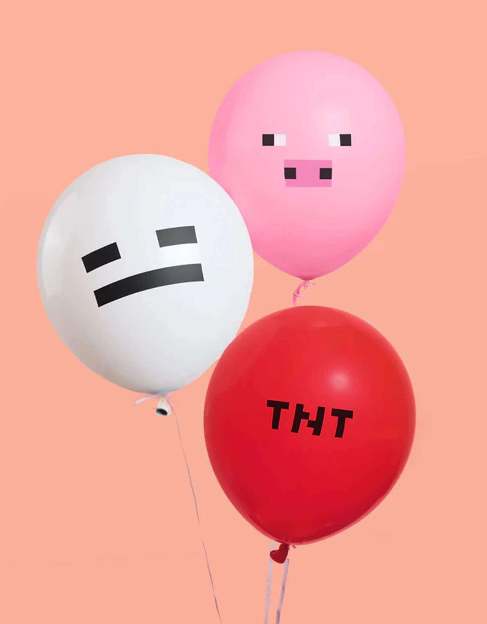 Three 11" Minecraft themed latex balloons in pink, red and with with pink pig face and ghost facial expression and TNT text on them on a pink background.