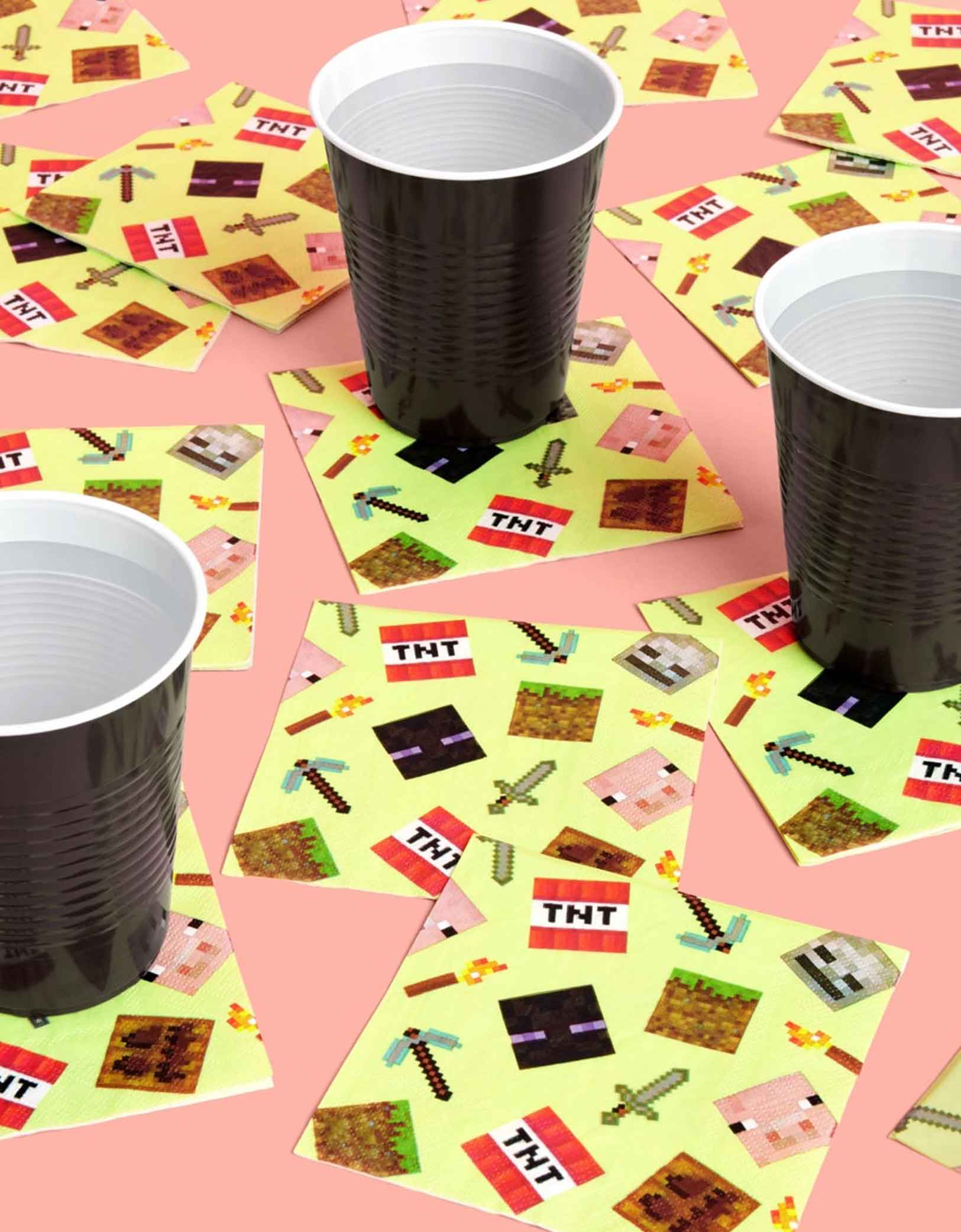 Black plastic cups on colorful placemats with Momo Party's 5" x 5" Minecraft-themed decorative paper napkins with pixelated icons scattered across on a pink background.