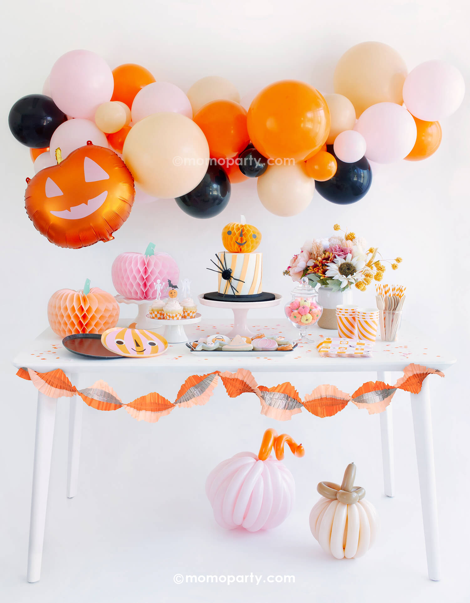 Momo Party's "Hey Pumpkin" Halloween party box featuring adorable pumpkin themed party supplies including a boo-tiful balloon garland in orange, pink, blush and black colors, smiley pumpkin shaped plates, groovy Halloween checkered napkins, honeycomb pumpkin decorations in pink and peach colors, with the pink and orange crepe streamer hung around the table and two boho colored pumpkin made with twisting balloons, this party look is perfect for a girly, kid's friendly pink Halloween bash this season!