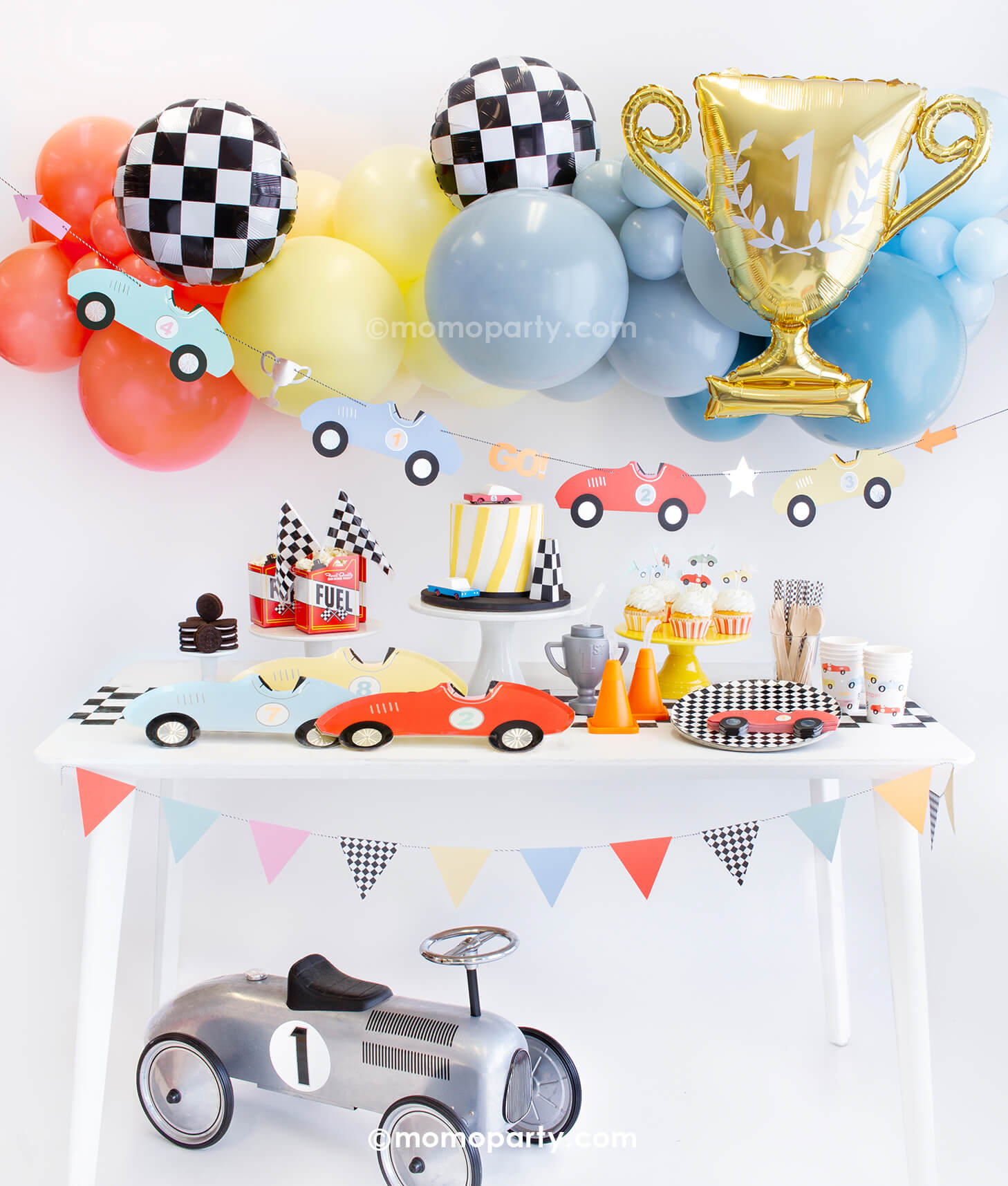 Momo Party Race Car Box featuring Meri Meri race car paper plates, race car shape napkins, race car graphic party paper cups, checkered round side plates, race car cupcake kit, candy car as cake topper, Fuel treat favor box with popcorns as tableware, colorful balloon cloud, race car party garland in pastel colors, checkerboard foil balloons and a trophy shaped foil balloon as decorations, all makes a great inspo for kid's modern race car party or a "Fast One" first birthday celebration.