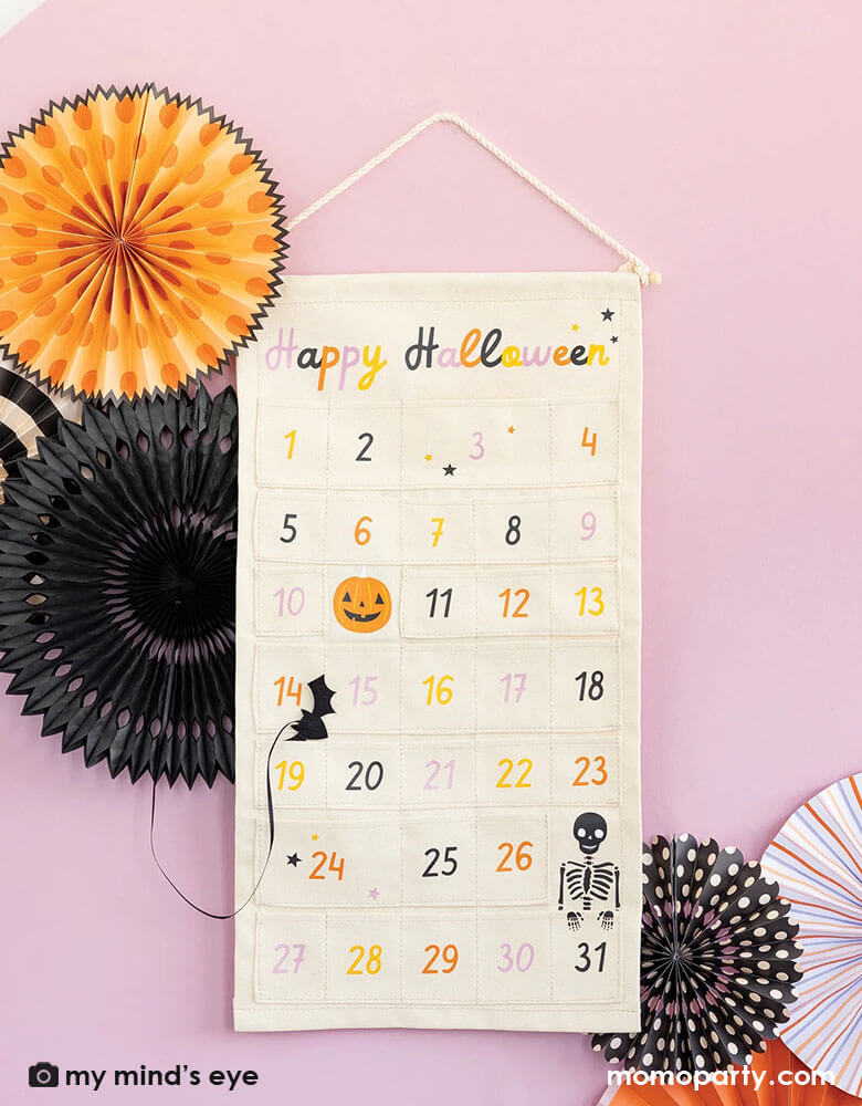 A wall decorated with Momo Party's Halloween countdown calendar with adorable Halloween character illustrations including pumpkins, skeletons, bats and more. Count down the days to Halloween with this spooky advent calendar! Perfect for kids and fun-loving adults, it features 31 canvas pockets - perfect for decorating your home with a little extra seasonal flair! Get ready for a wickedly fun Halloween countdown!
