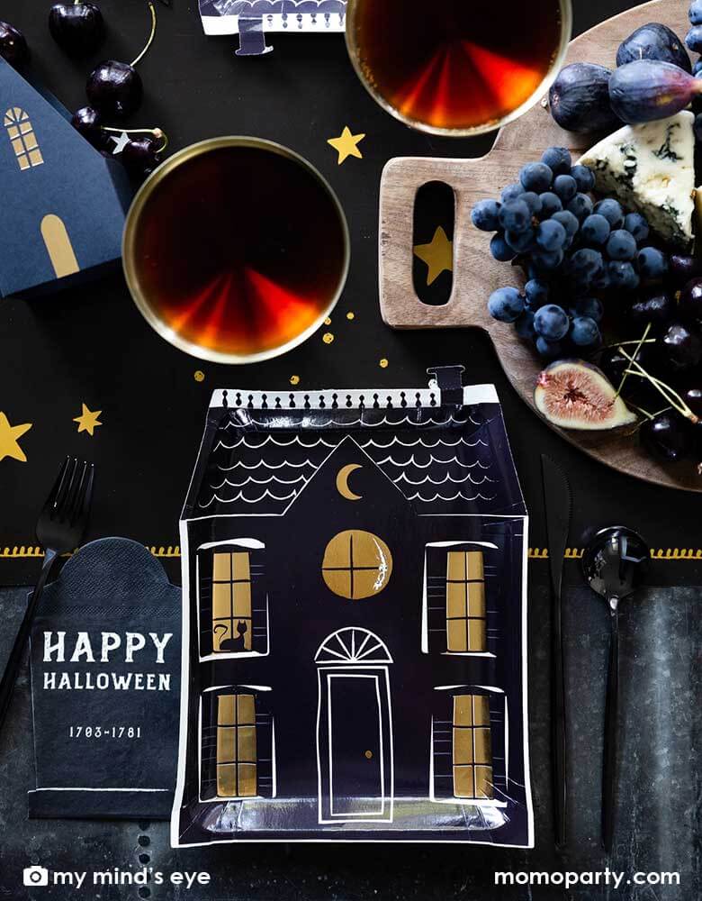 A black and gold Halloween tablescape featuring Momo Party's 8" x 10.5" haunted village haunted house shape plates and black tombstone shaped napkins with Happy Halloween words on them. Around the tableware, there are red drinks and black themed charcuterie board on Momo Party's mystical dark night table runner, gives a spooky vibe to an elegant Halloween tablescape.