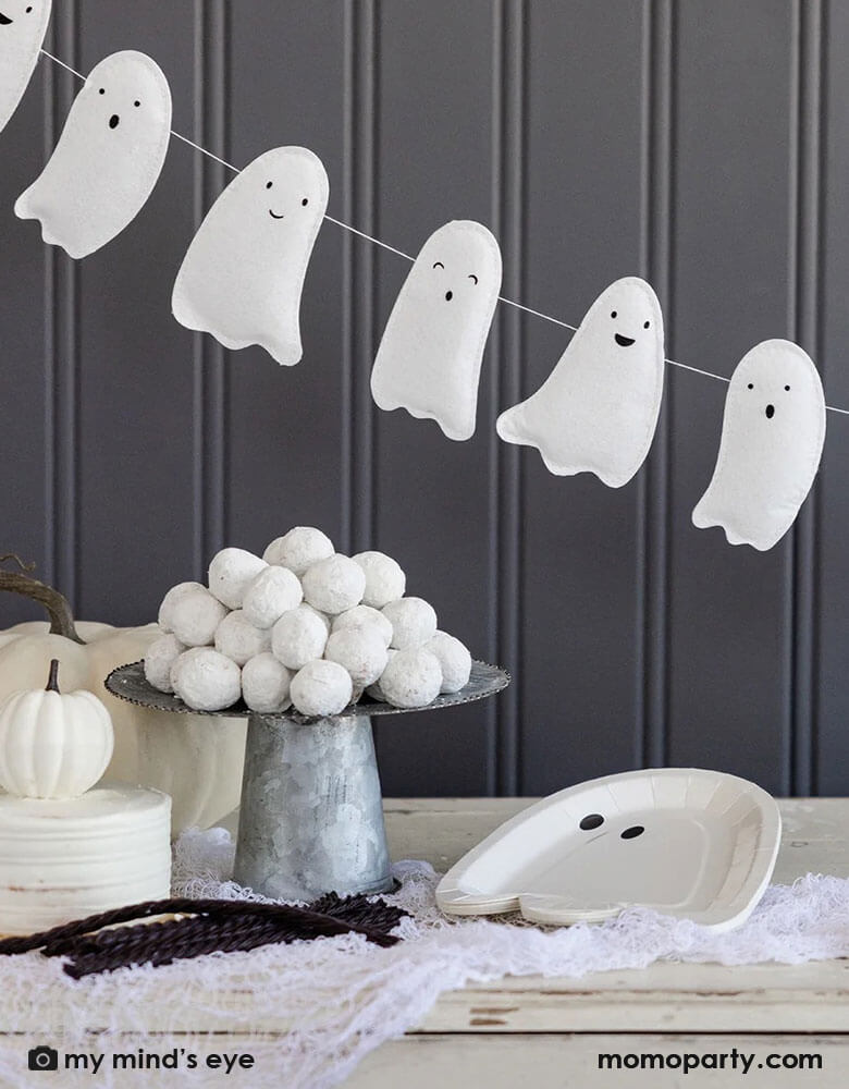 A gray farmhouse wall decorated with Momo Party's 6f puffy ghost shaped banner in front of a dessert table which is filled with ghost shaped plates, a bowl of white donut holes, and some white pumpkins around. Makes it a simply yet cute Halloween home decoration inspiration.