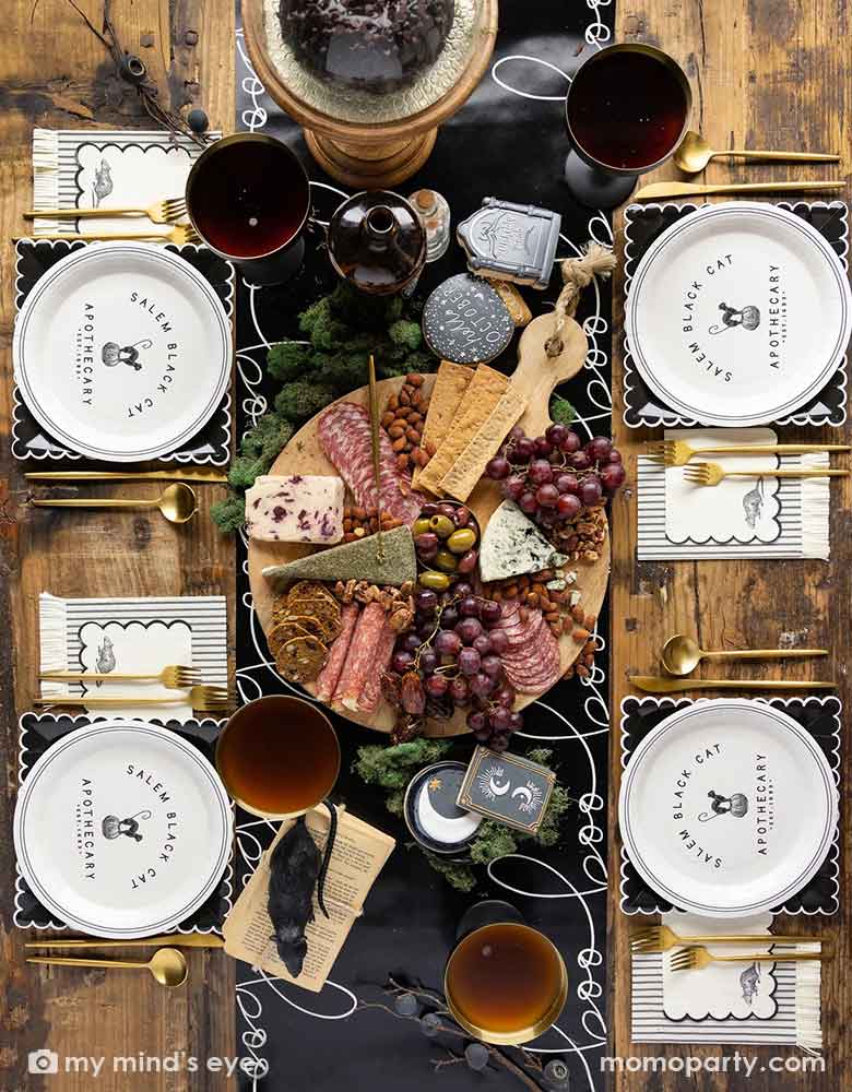 A elegant chic Halloween tablescape featuring Momo Party's Salem-Apothecary-Halloween-party supplies including black and white round plates with black cat design, black scalloped white edged plates and Salem Apothecary Black Ticking Fringe Dinner Napkins by My Mind's Eye. On the table there is Salem Apothecary Boo Table Runner with Halloween themed crescent moon sugar cookies and a charcuterie board board. Makes it a great inspo for an elegant Halloween table.