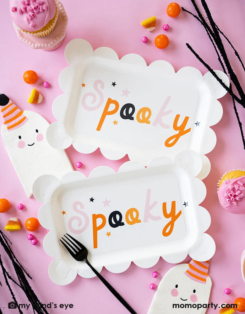 A pink Halloween party table features Momo Party's 11.5" x 7.5" Spooky scallop edged plates and ghost with a party hat shaped napkins, around the tableware there's pink cupcakes and pink Halloween treats including candy corns, orange gum balls and pink candies, all makes a great inspiration for kids not-so-scary Halloween party ideas.