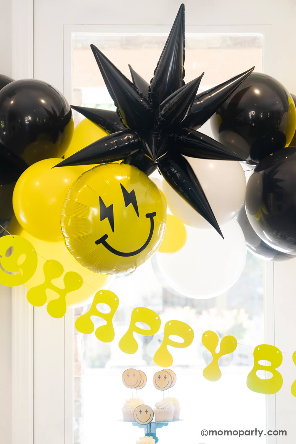 A close-up look at Momo Party's 'Cool Dude' themed Birthday Party. Featuring a captivating balloon garland in black, white, and yellow, accented by a black starburst foil balloon and a smiley face foil balloon with lightning bolt eyes. This stylish decor is complemented by a retro neon happy birthday banner. Perfect for a boy's 'One Happy Dude' themed first birthday, a 'Two Cool' themed second birthday party, 'Ten Rad Years' 10th birthday celebration, or kids birthday party for all ages.