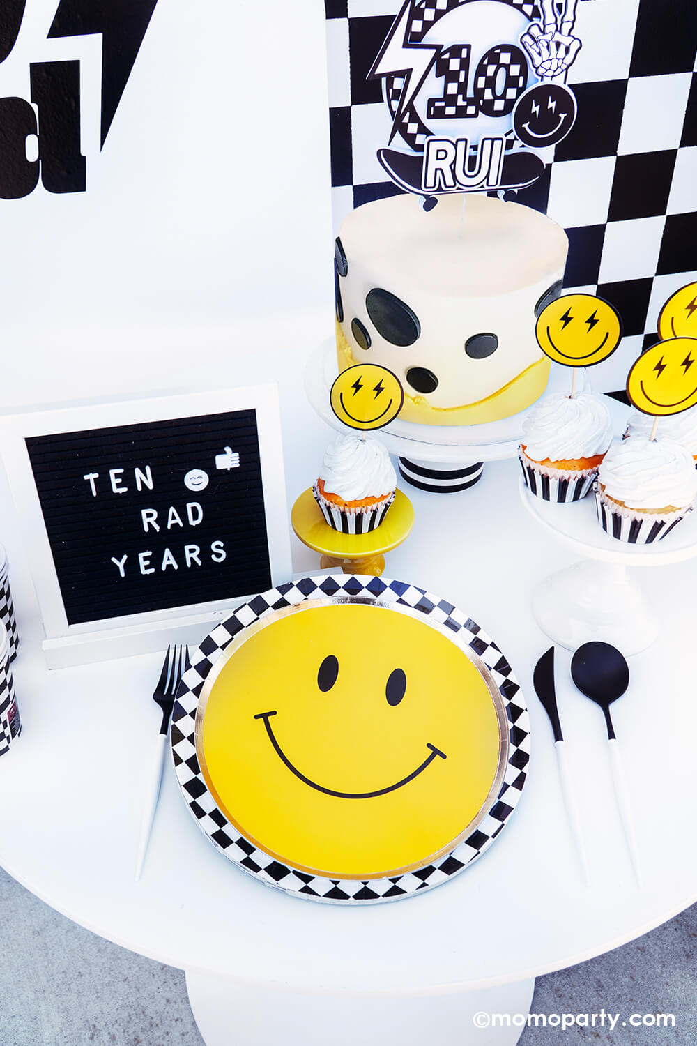 Boy's "Ten Rad Years" 10th birthday party tablescape by Momo Party. Featuring the classic black and white checkered patterned plates, cups, napkins and smiley face plates, this rad party table decoration is perfect for your cool dude's very first double digits party! With a mix of cool dude aesthetics, smiley-face accents, and checkered patterns in black and white, we've got the perfect recipe for a memorable boy's birthday bash. Don't miss out on making this party as special as your rad boy.