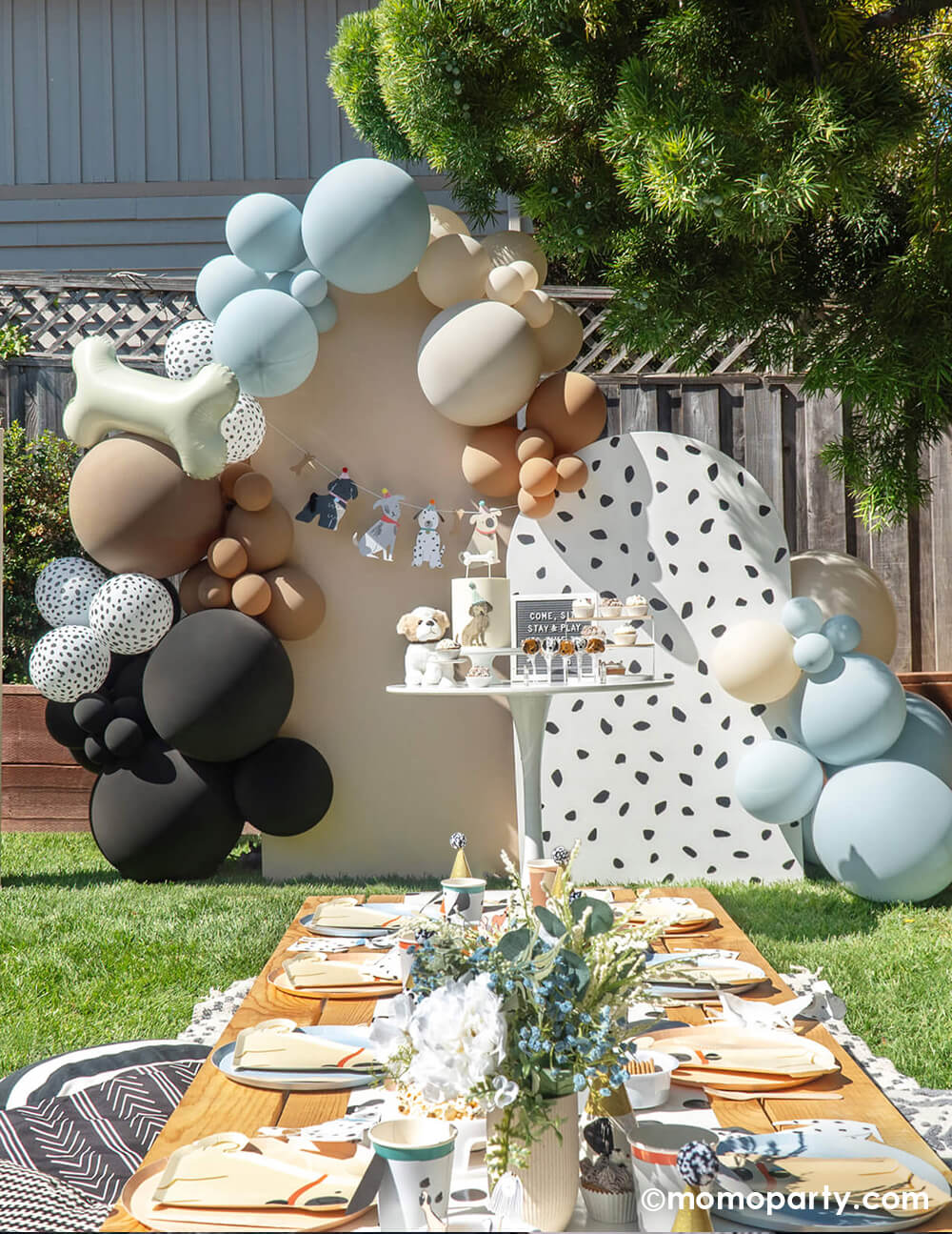 Momo Party's It's Paw-ty Time Puppy Themed Birthday Party, with a kid's picnic table in the front, Dog themed cake, cupcakes, letterboard and puppy toy on the a dessert table, in front of lots of Latex Balloons in Black, Mocha, Dots, Fog, and Stone colors, around a blush and dots wooden board as backdrop, there are Dog Bone shaped foil balloon on it for a modern elegant puppy themed birthday party