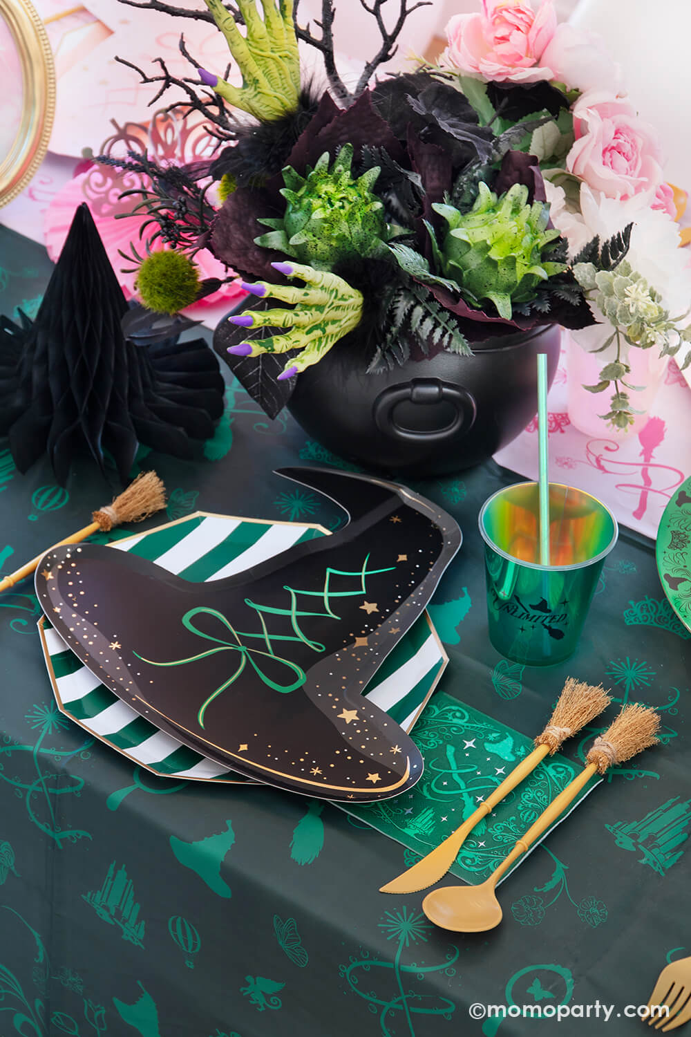 A Wicked themed party table setting with various of Momo Party's Wicked themed party supplies including the wicked witch hat shaped plate, emerald green striped dinner plate, the Wicked green napkin inspired by Elphaba, witchbroom shaped utensil set, and wicked green party cup with green iridescent straw on the green and pink two-tone Wicked tablecloth. With Wicked inspired floral bouquet and witch hat honeycomb centerpiece, it makes a whimsical and mystical Halloween celebration in this spooky season!