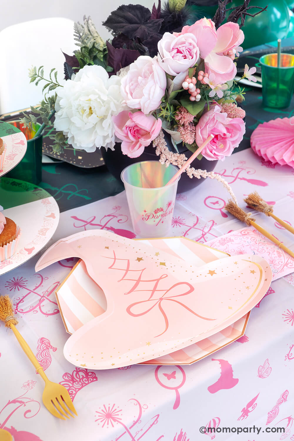One side of Wicked themed party table setting inspired by Glinda with various of Momo Party's Wicked themed party supplies including the pink witch hat shaped plate, pink striped dinner plate, the Wicked pink napkin inspired by Glinda, witch broom shaped utensil set, and Glinda pink party cup with pink iridescent straw on the pink and green two-tone Wicked tablecloth. With Glinda inspired floral bouquet, it makes a great setting for an enchanting Wicked themed celebration.