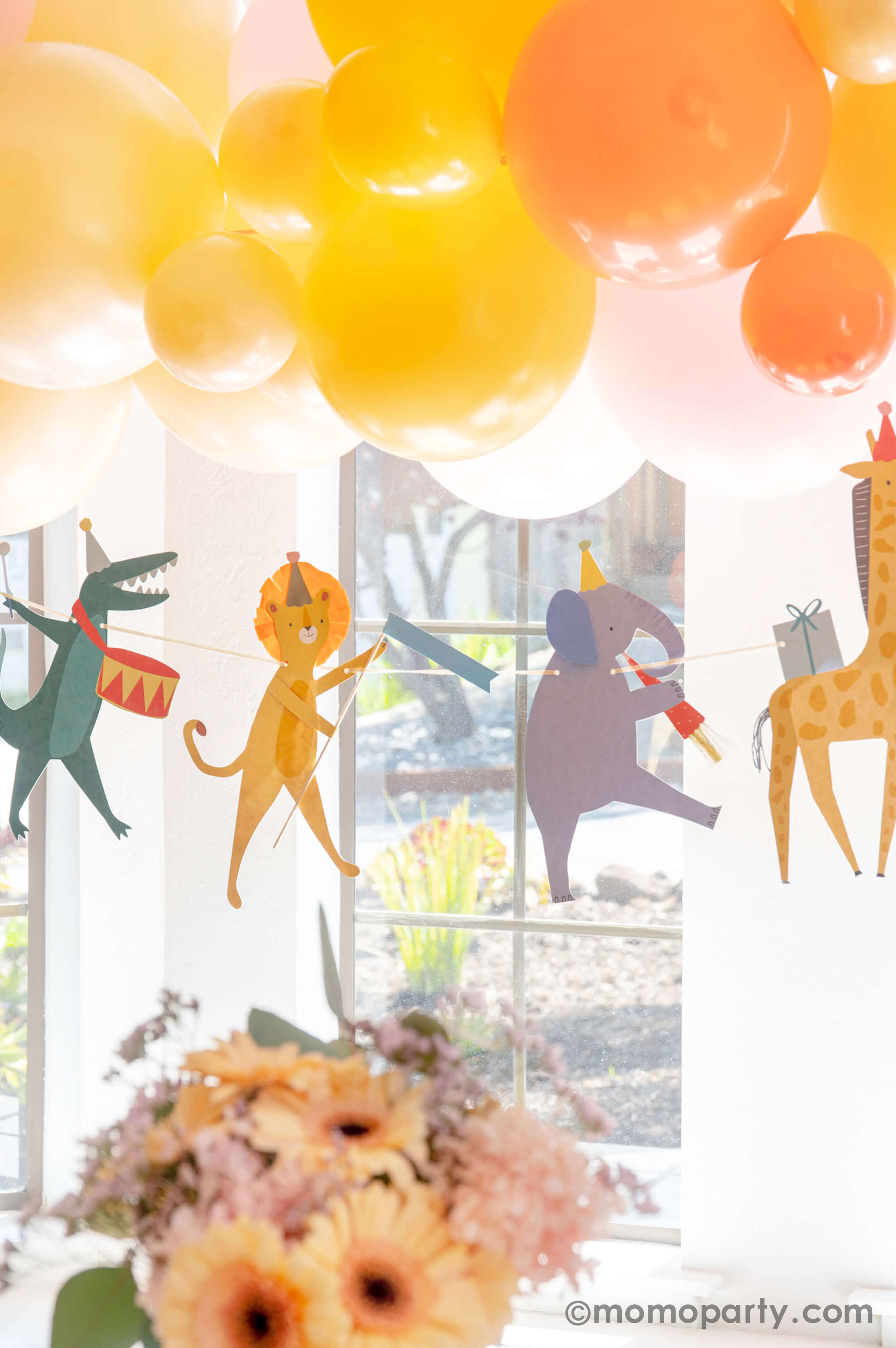 A kid's animal themed party decoration idea featuring Momo Party's adorable animal parade birthday garland featuring a lion, an elephant, an alligator, a giraffe, along with a festive balloon garland in a warm color tone in the back, it makes a great party inspiration for kid's animal, safari, carnival themed birthday party.