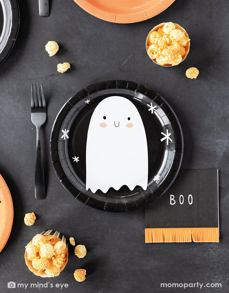A kid's friendly Halloween party tablescape features Momo Party's classic Halloween party supplies including the friendly ghost black round plate, the boo fringe small napkins, and the orange and black striped food cups filled with popcorn. This simple and modern place setting provide an effortless yet festive idea for celebrating Halloween with kids this spooky season.