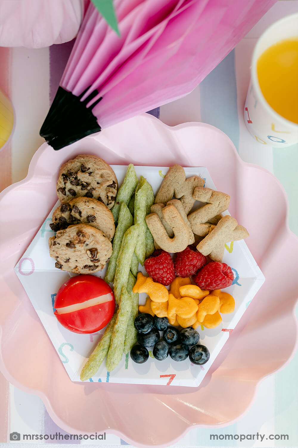 A pastel back to school party table food snack ideas by Mary at Mrs Southern Social. Featuring Momo Party's back to school party supplies including ABC alphabet plates, napkins, and party cups. One the plates are kids snack ideas including fruits, cheeses, goldfish, ABC alphabet crackers. With pastel rainbow striped placemats and pastel rainbow pencil honeycombs and pink apple honeycombs, all together makes an adorable tablescape for kid's first day of school celebration.