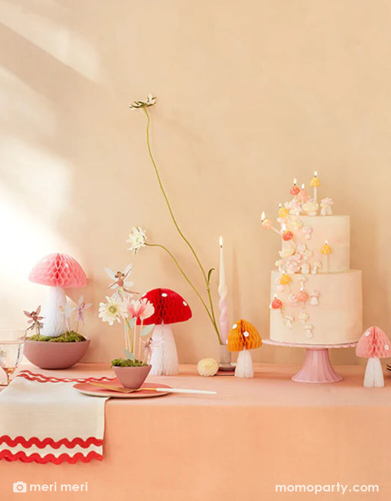 A whimsical fairy themed birthday party table featuring Momo Party's mushroom honeycombs and fairy cake toppers. A 2-tier cake is topped with mushroom candles and adorn with buttercream flowers, makes this a simple yet whimsical party inspo for kid's forest fairy themed party.