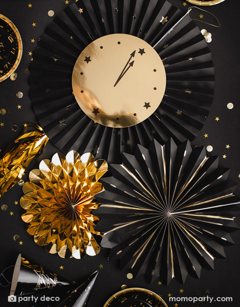 A black party table filled with confetti and new year party hats around Momo Party's New Year Countdown Party Fans by Party Deco. Comes with 3 party fans in the size of 26 cm, 35 cm, 43 cm in gold and black, this paper fan set with a paper clock on it is perfect for your New Year's Eve Countdown party.