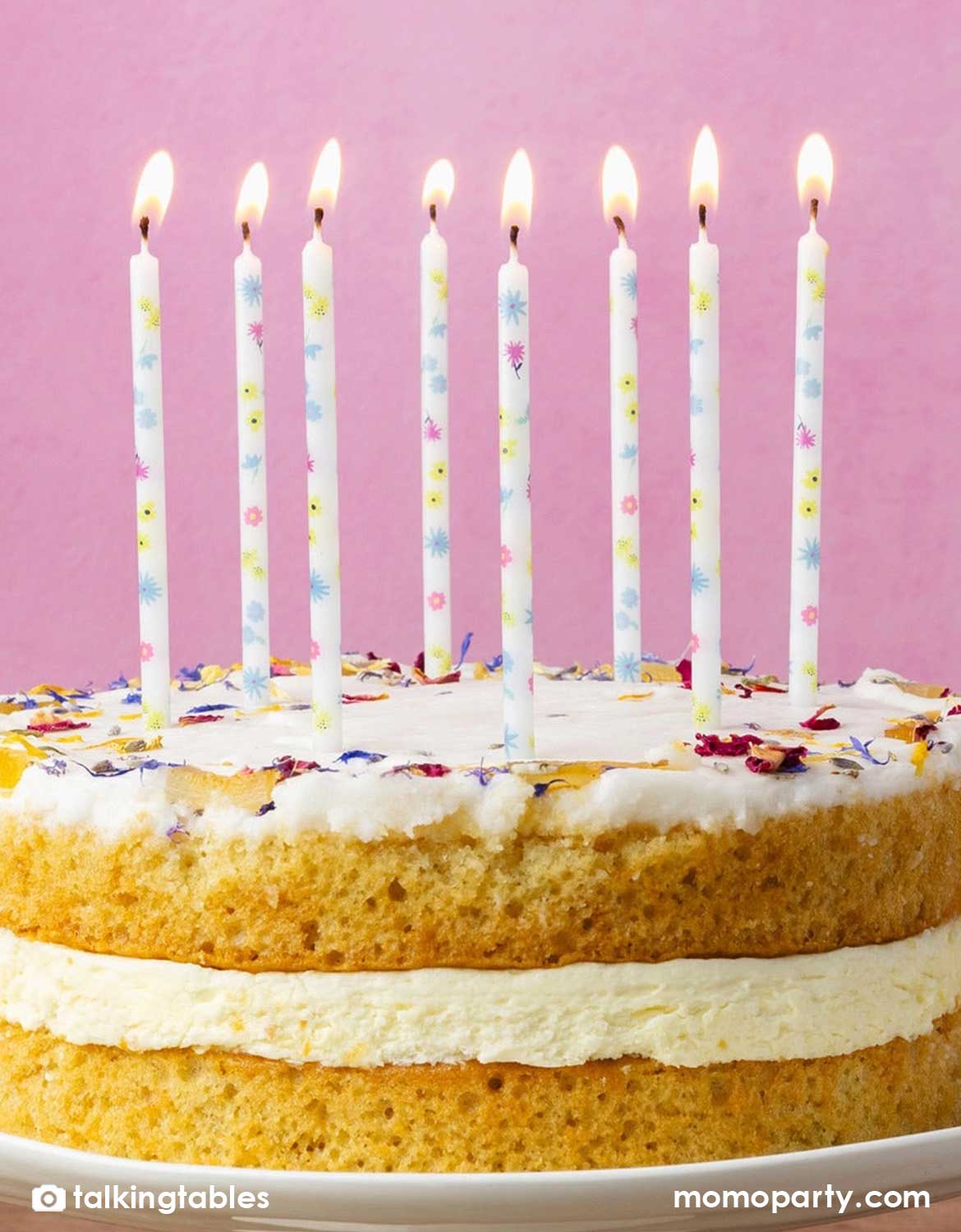 Momo Party's set of birthday candles with pastel floral designs on a birthday cake decorated with flower pedals against a pink background.