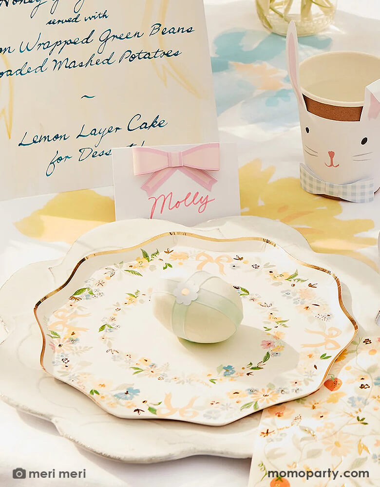 A spring Easter themed party table featuring Momo Party's Elegant Floral Party Collection including Meri Meri elegant floral Dinner and side plates, napkins and bunny shaped plates, on the table there are spring flowers, Easter inspired cupcakes, bunny shaped party cups and bunny shaped party crackers, and Pastel Bow Place Cards, makes this a perfect inspo for an elegant Easter celebration.