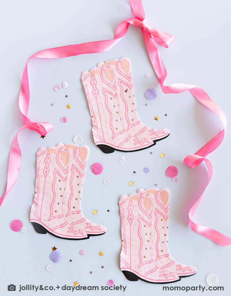 Momo Party's 7.25 x 6.25 inches Cowgirl Boots Shaped Large Napkins by Daydream Society on a light lilac table. Around the napkins are some pastel colored confetti and small gold foil star shaped confetti. Around the napkins, a pink ribbon tied a bow on the top and the tails wrapped around the napkins, making this a great inspo for a girl's pony themed birthday decoration.