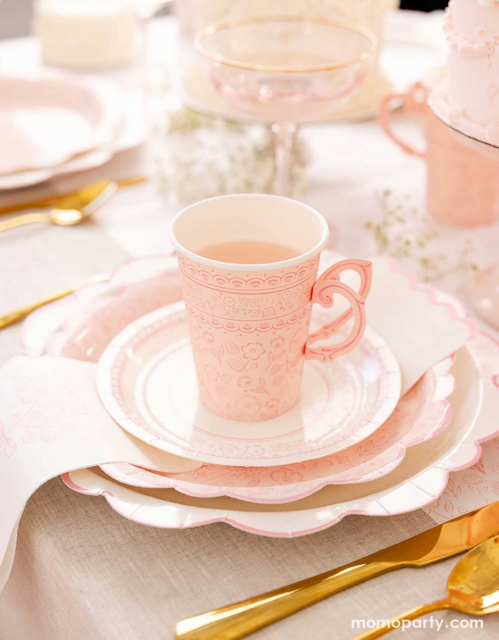An elegant placeset featuring Momo Party's Pink Pembroke tableware collection including the 12" Pembroke Pink Edge Scallop Plates paired, 9" Pembroke Pink floral Plates, 7" Pembroke Pink Plates, Pembroke Pink napkins and the 12oz party cups. Underneath the plates is the Pembroke Pink floral paper table runner. With the gold foil utensil set, a pretty floral arrangement and pastel pink butter cakes and glasses of rose champagne, this table setting is perfect for a spring Easter inspired celebration.