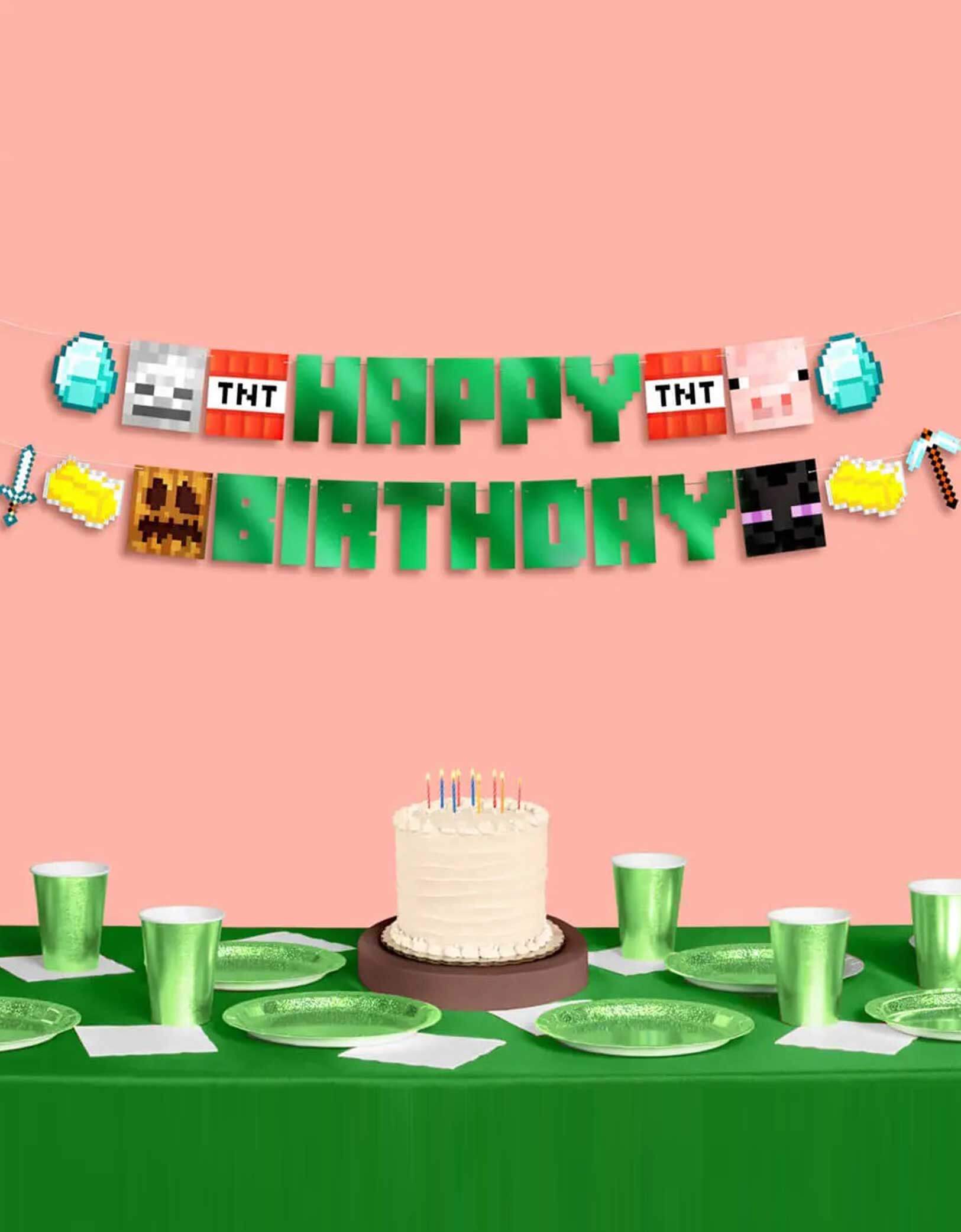 A Minecraft themed birthday party setup with Minecraft-themed decorations including a party banner and tablewares from Momo Party, with a birthday cake on a green tablecloth covered table on a pink background.