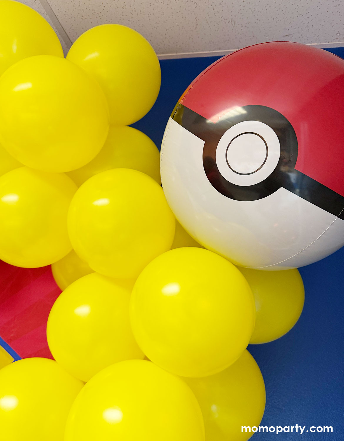 A kid's Pokemon themed birthday party decoration by Momo Party featuring a red, black, and yellow latex balloon garland and Pokeball foil balloons with a 'Happy Birthday' banner sign.