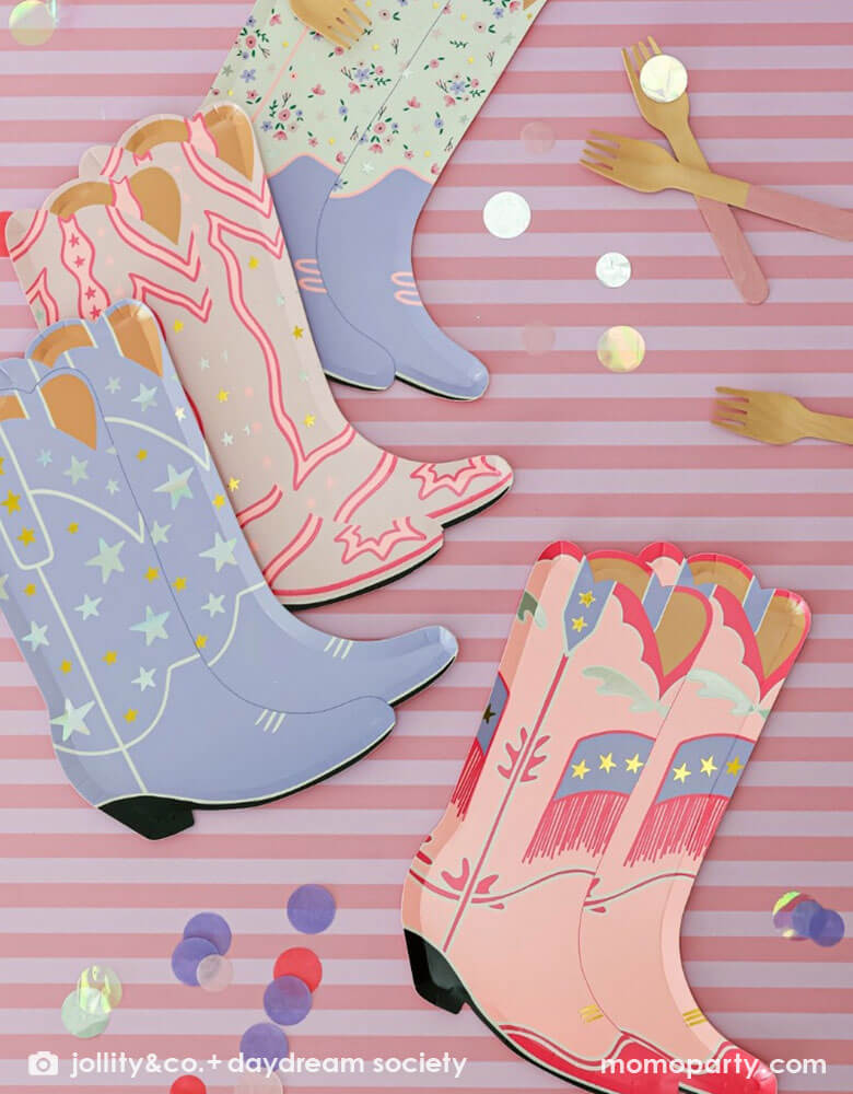 An overhead shot of Momo Party's 8" x 6" Pony Tales Large Boot Shaped Plates by Daydream Society with pink striped background and confetti and pink utensils around. Comes in a set of 8 cowgirl boots shaped plates in 4 different designs and colors, these plates feature pink and purple boots trimmed with gold and silver foil details are perfect for a Western cowgirl themed party or girl's horse/pony themed birthday celebration.