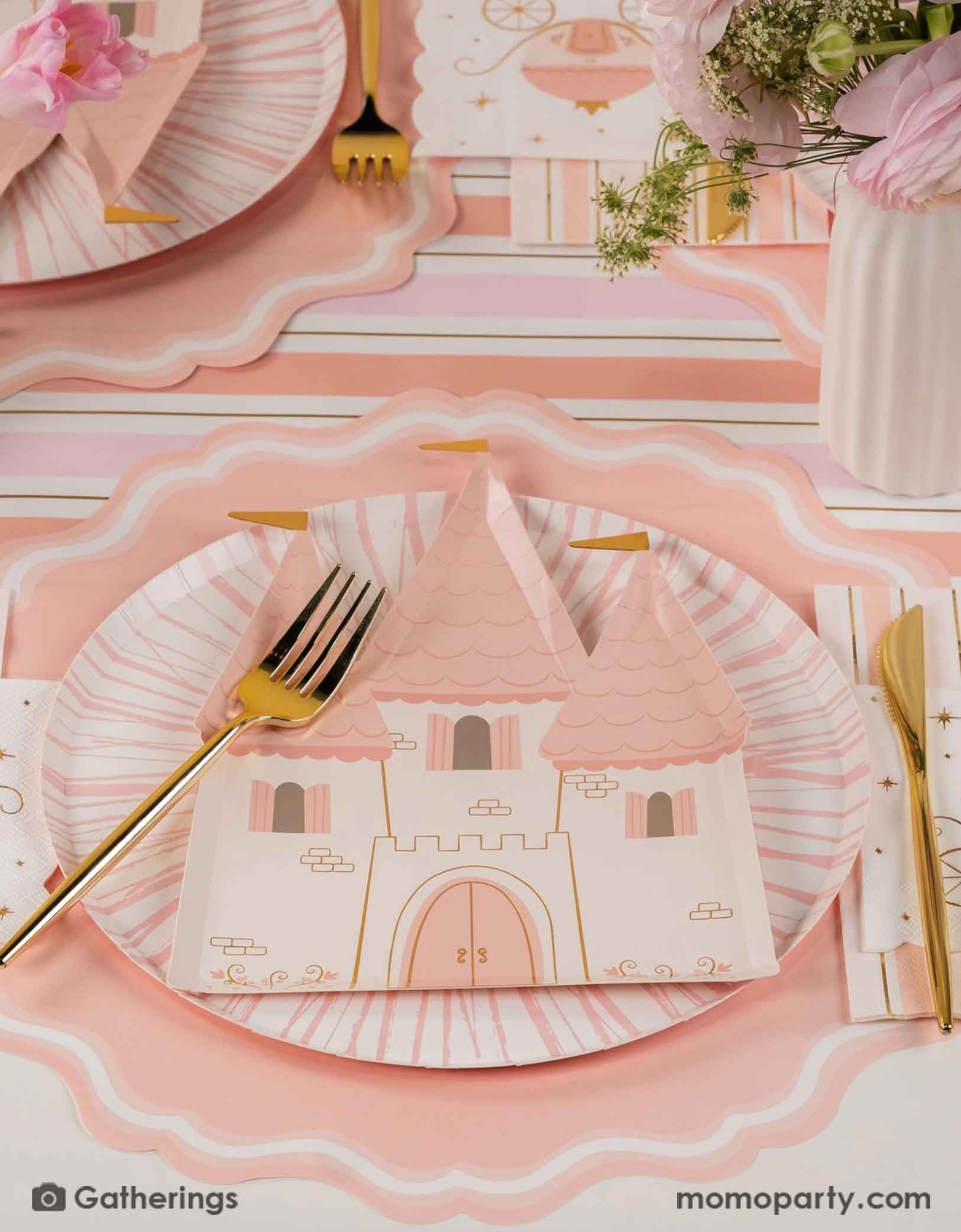 A beautiful princess themed table setting featuring various princess themed party supplies from Momo Party's including the castle shaped plates, princess carriage small napkins, gold cutlery, castle shaped treat box, and the pink and gold striped table runner, with pink beautiful floral bouquet on the table, this creates a fairy tale tablescape for a girl's princess themed birthday party.