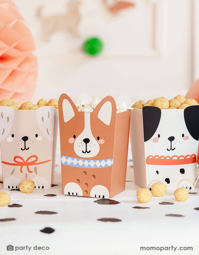 An adorable dog puppy themed birthday party table featuring Momo Party's Puppy Dog Party Snack Treat Boxes by Party Deco. These snack boxes come in 4 designs of different puppies with adorable dog design on it. They're filled with popcorn, chips and treats placed on the Dalmatian printed dot tablecloth underneath, with pastel honeycomb decorations around the table and a happy birthday banner in the back, this makes a cute scene for kid's dog themed birthday party celebration.