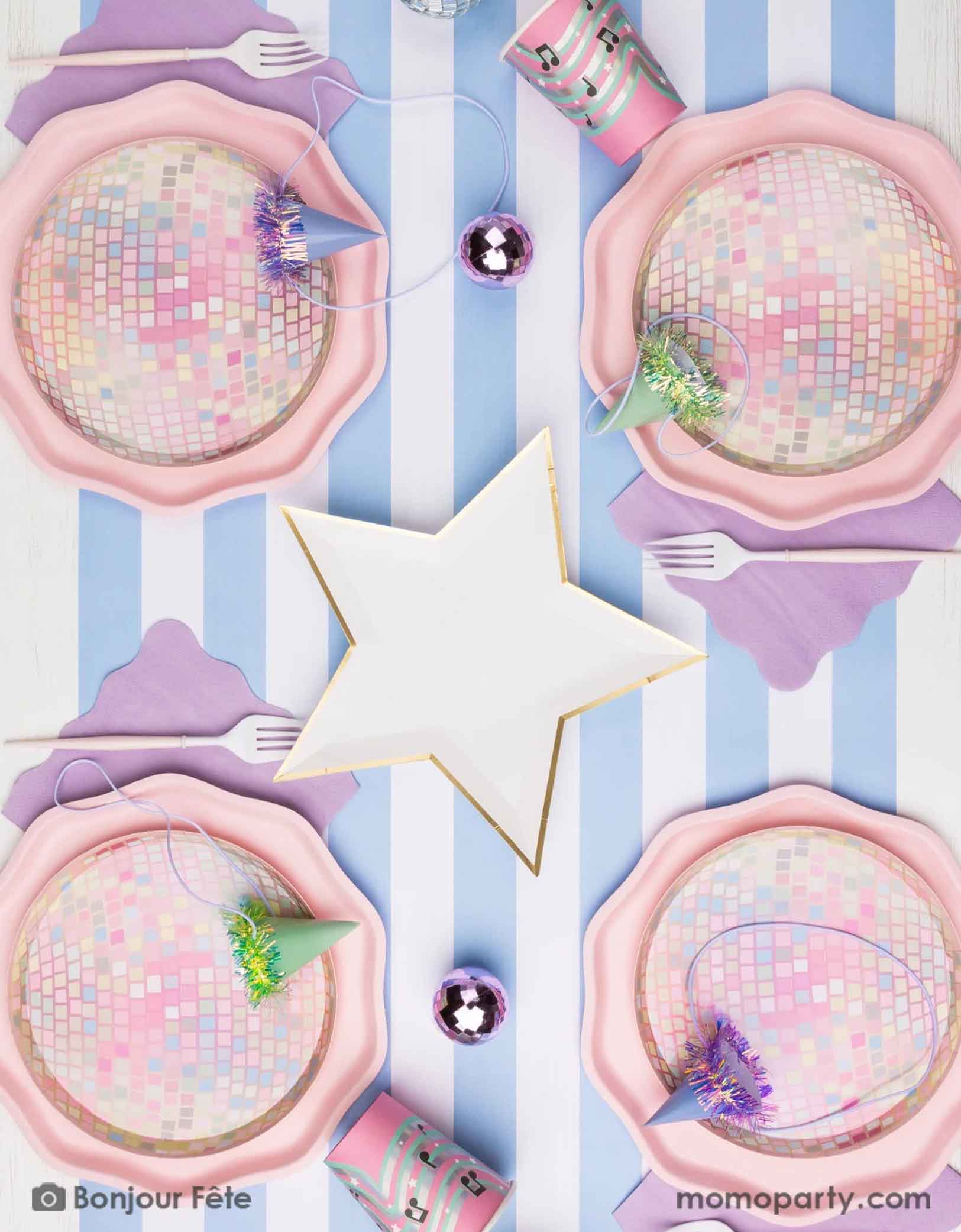 An overhead shot of a disco ball and star inspired pastel table setting featuring Momo Party's 8" pink disco ball shaped plates with star decorations and music note pink party cups on a blue striped table runner. Perfect for kid's rock star or pop star themed birthday party.