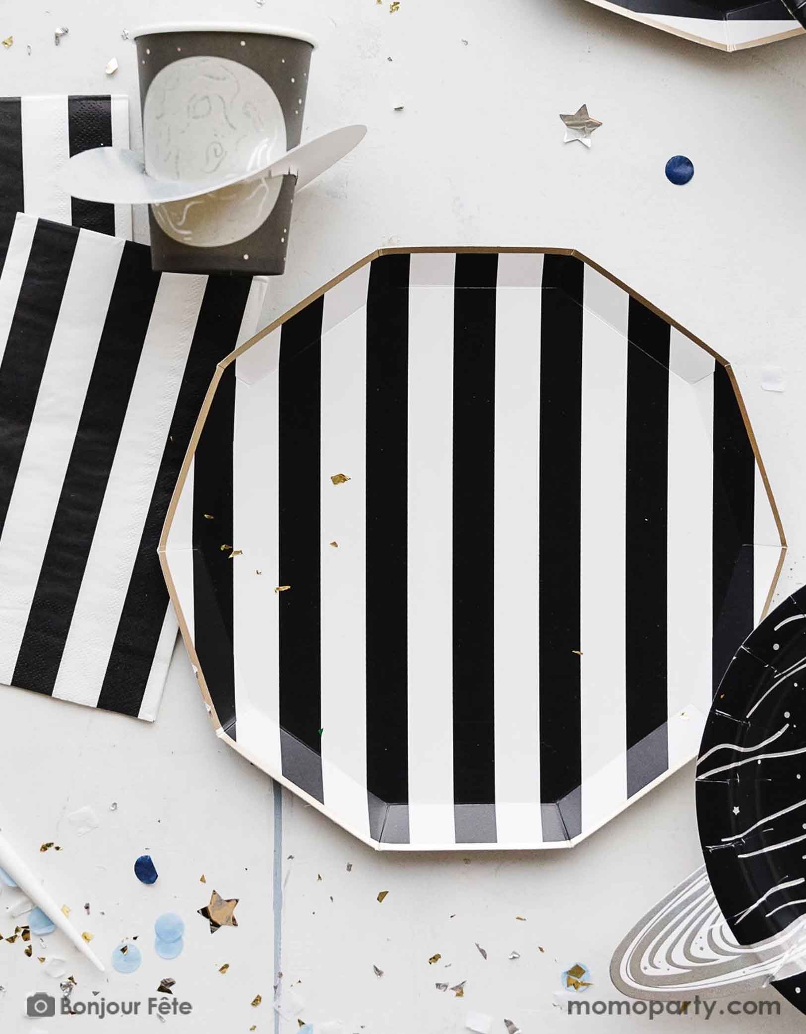 A space themed party table featuring Momo Party's Black Striped Party Supplies including paper dinner plates, guest towels, black and white cutlery set. With the planet 3D party cup and metallic star confetti around the table, this makes a perfect inspo for a chic, stylish and modern space themed celebration.
