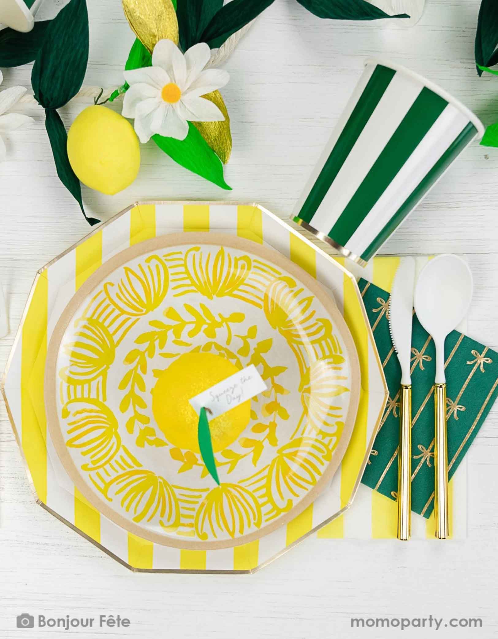 An elegant summer Capri lemon themed party tablescape featuring Momo Party's cabana striped party tableware in yellow and green including table plates, cups and napkins. On the table there's a summer party garland with flowers, greenery, lemons as decorations.