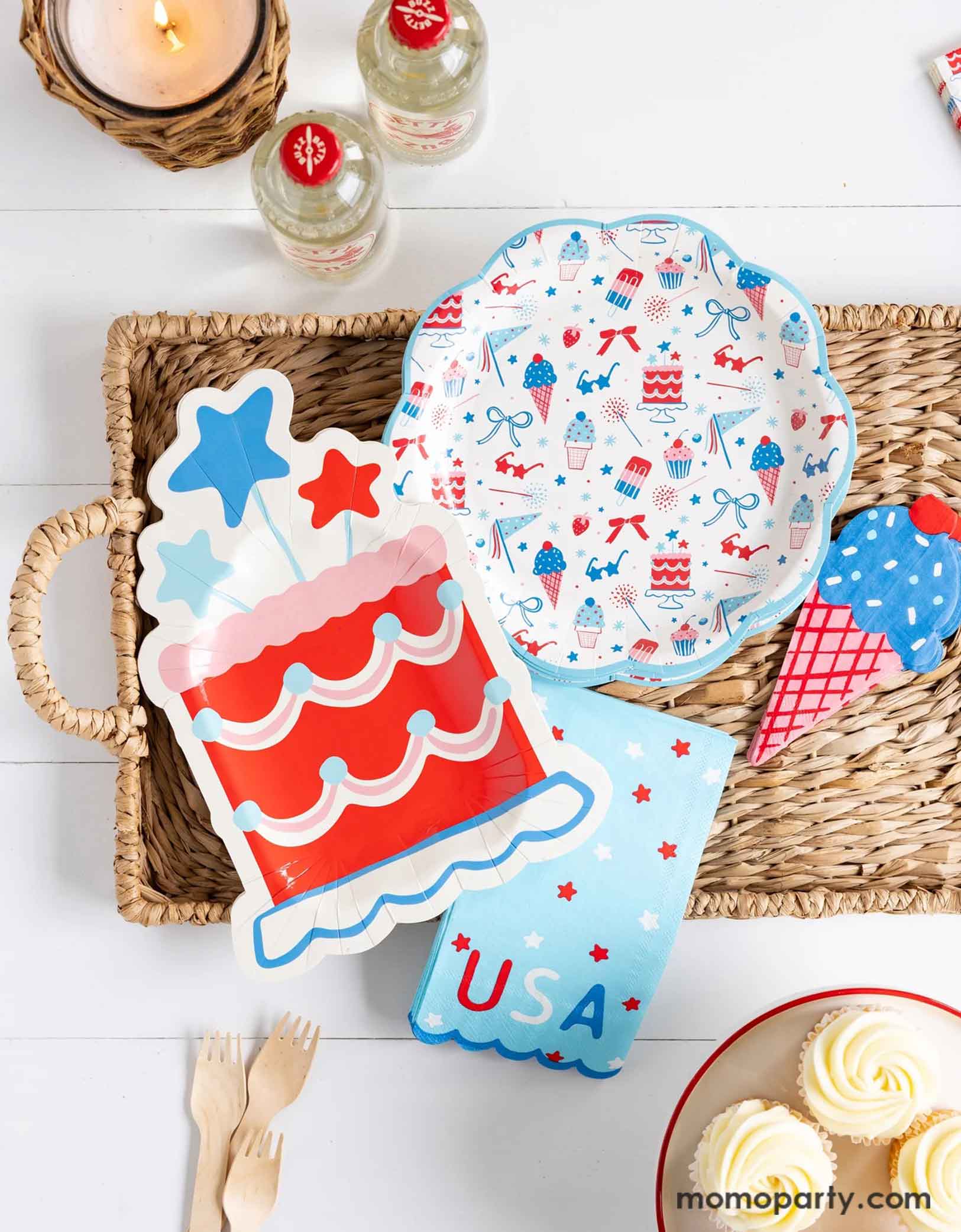 An overhead shot of a patriotic themed celebration featuring Momo Party's Summertime pattern plates, napkins, cake shaped paper plates, and ice cream shaped dinner napkins on bamboo woven tray. Around the tray there are some white buttercream cupcakes, some wooden forks and a couple of soda bottles in red, making this a great party inspo for a Fourth of July party, a Memorial Day BBQ or any patriotic summer celebrations!