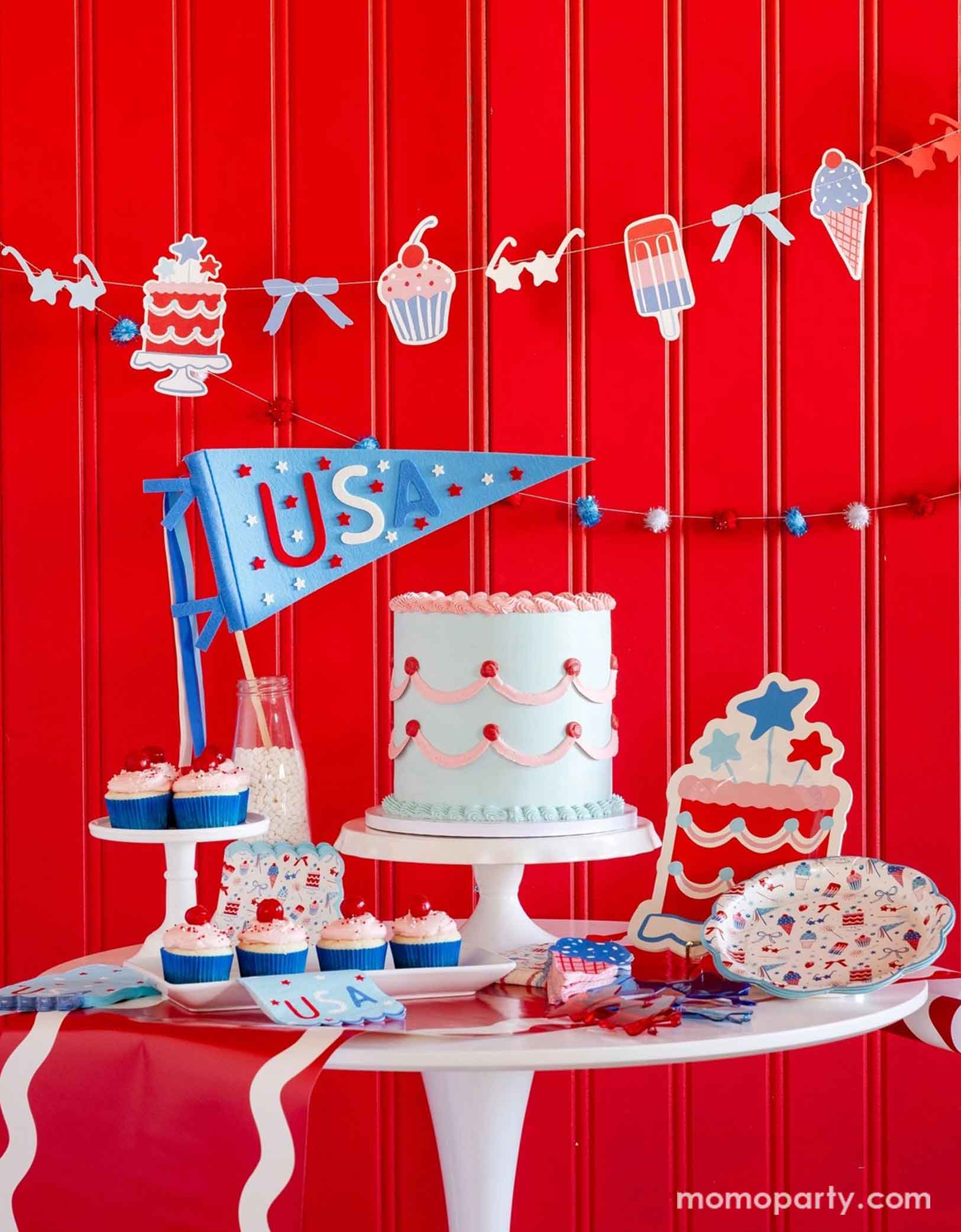 A festive patriotic party set up featuring various Fourth of July themed party decors from Momo Party including party banner with summer themed party pennants including popsicles, ice cream, cupcake, cakes, and star shaped sunglasses in red, blue and white colors. On the table there's a vintage pastel blue buttercream cake along with some cupcakes with cherries on top, along with a USA felt pennant and patriotic party tableware including party plates, napkins and a table runner, for a fun summer party.