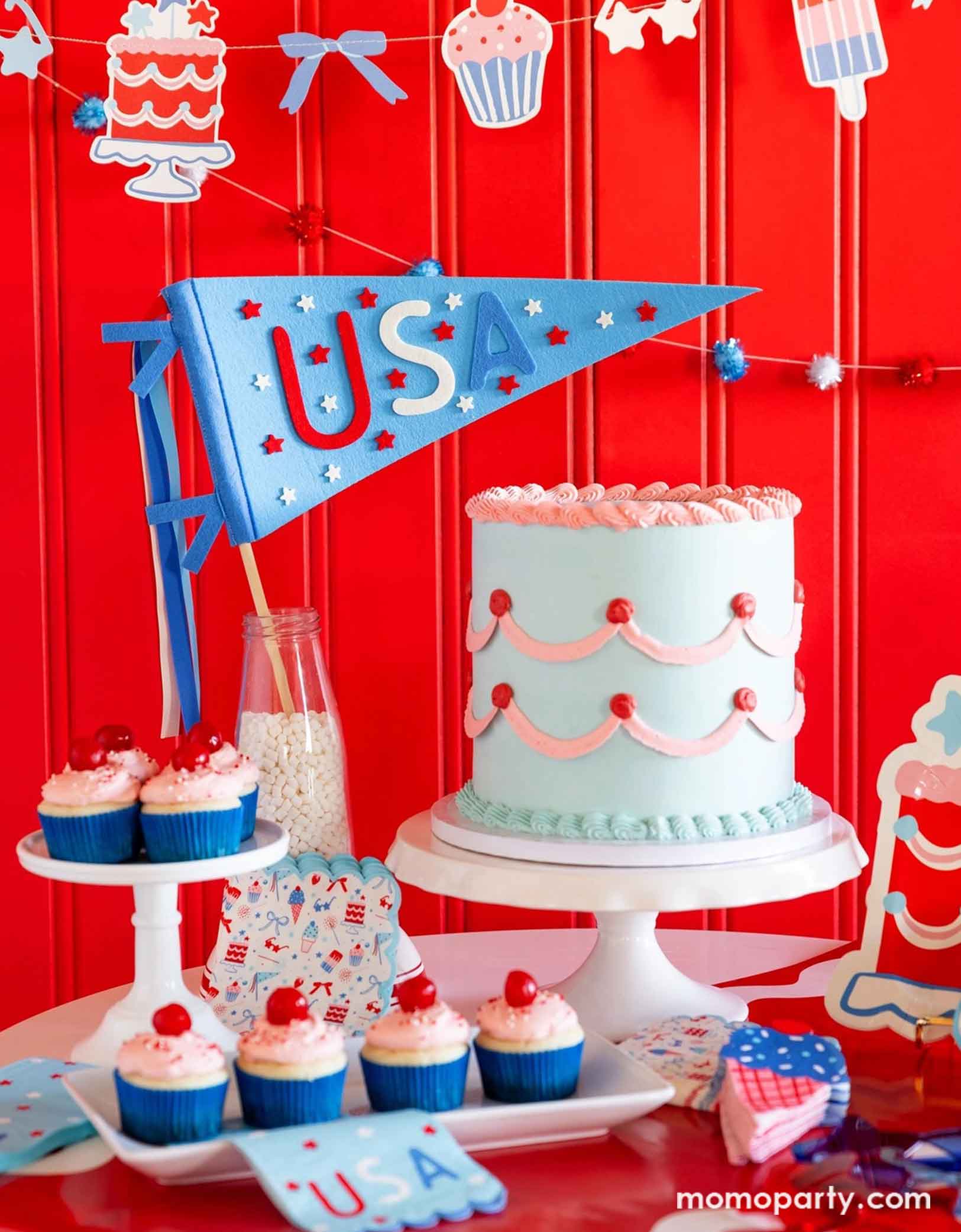 A festive patriotic party set up featuring various Fourth of July themed party decors from Momo Party including party banner with summer themed party pennants including popsicles, ice cream, cupcake, cakes, and star shaped sunglasses in red, blue and white colors. On the table there's a vintage pastel blue buttercream cake along with some cupcakes with cherries on top, along with a USA felt pennant and patriotic party tableware including party plates, napkins and a table runner, for a fun summer party.