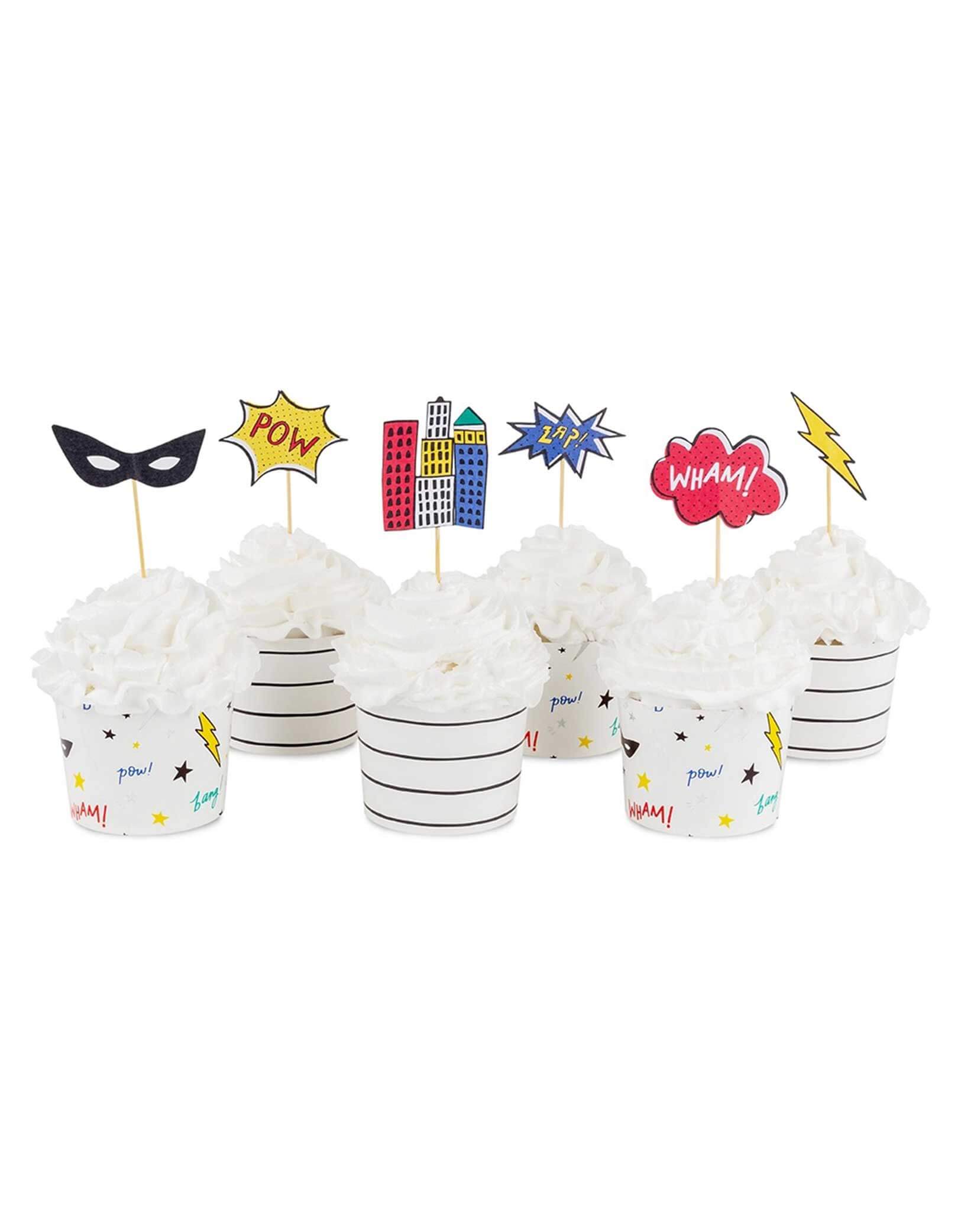 6 cupcakes decorated with superhero cupcake toppers with superhero-themed designs including superhero masks, city buildings, lightning bolt, and action words on sticks on a white background.
