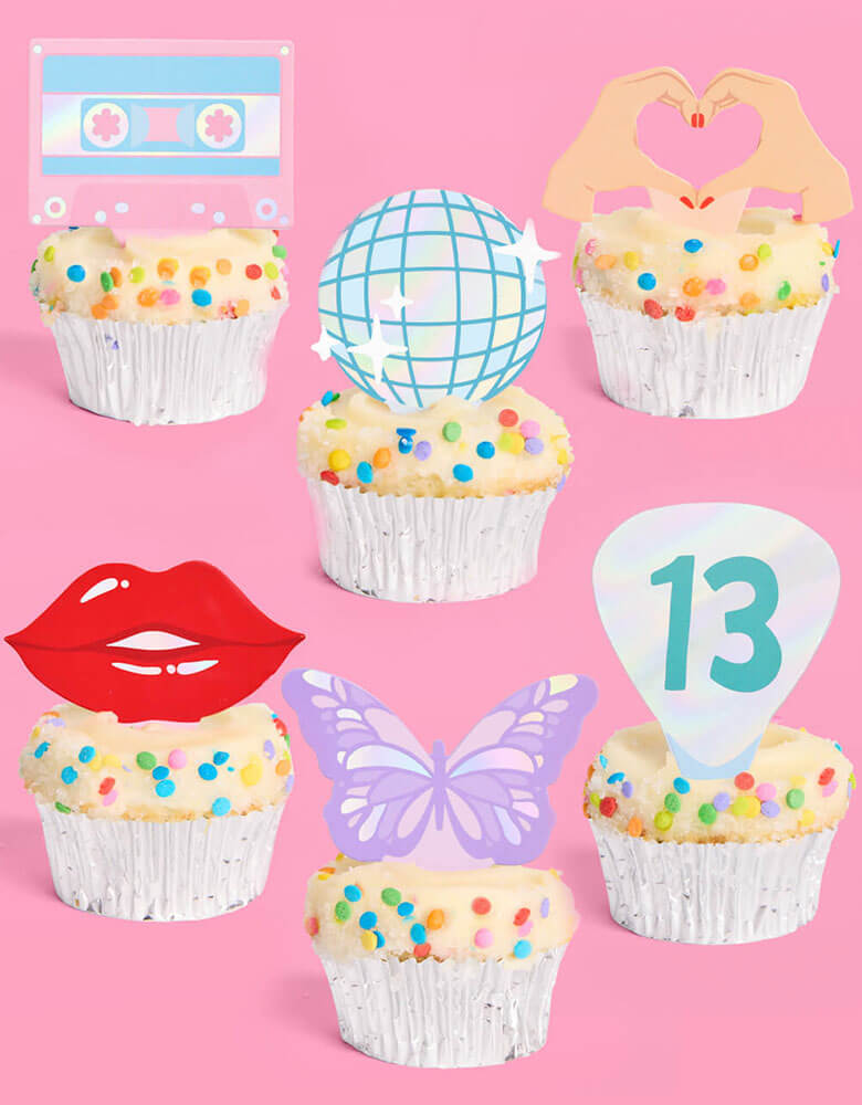 A few birthday cupcakes adorned with Momo Party's Era's Party Cupcake Toppers by Xo, Fetti. Comes in a set of 24, these Taylor Swift-themed dessert/cupcake toppers are with iconic designs including butterflies, red lips, disco balls, cassettes, guitar picks and heart hand symbols. They're perfect for to celebrate your Swiftie girl's special birthday.