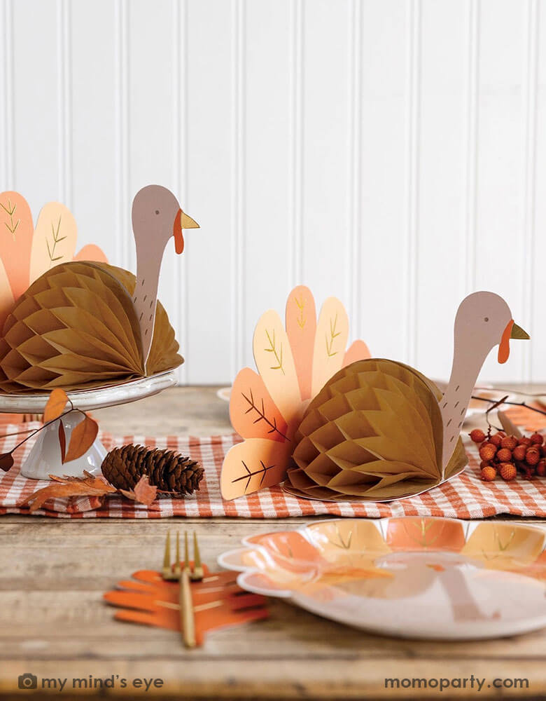 A fall inspired party table features Thanksgiving party supplies by Momo Party including the turkey shaped plates, oak leaf shaped napkins and turkey honeycomb decorations as the centerpiece. With some fall leaf and acorn decorations spread across, this makes a perfect inspo for an autumn gathering or Thanksgiving dinner decor this harvest season.