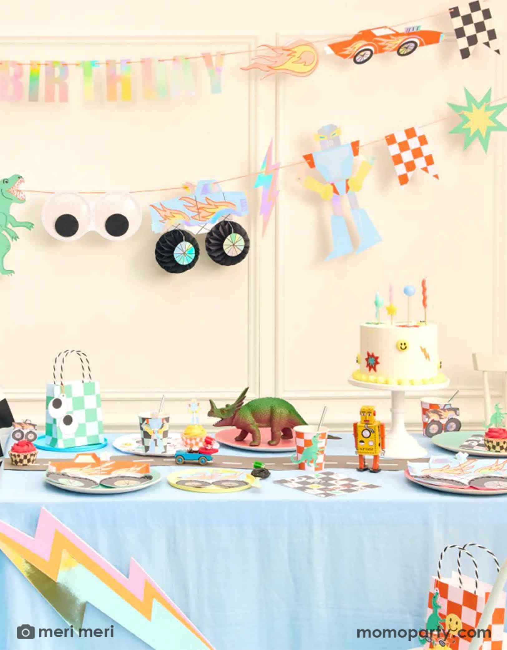 A fun themed kid's birthday party decorating set up featuring Momo Partys Momo Party's Toybox Party Collection by Meri Meri. With the retro inspired and checker board designs,  featuring elements from kid's toy boxes including dinosaurs, monster trucks, race cars, googly eyes. robots and lightning bolts, these party supplies including a large party garland on the way with HAPPY BIRTHDAY message, and a table of fun and festive party tableware including party plates, cups, napkins and favor bags.