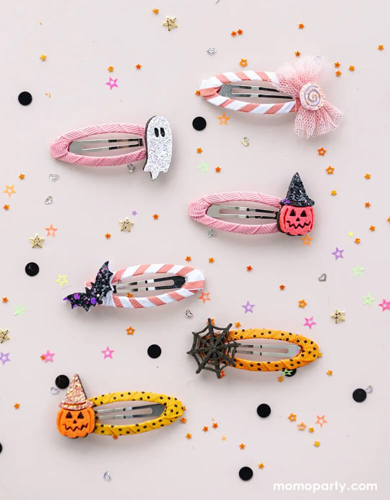 Momo Party's set of Halloween-themed hair clips with designs of a ghost, candy, pumpkin, spider web, bat in pink and peach designs on a light pink background with Halloween decorative elements.