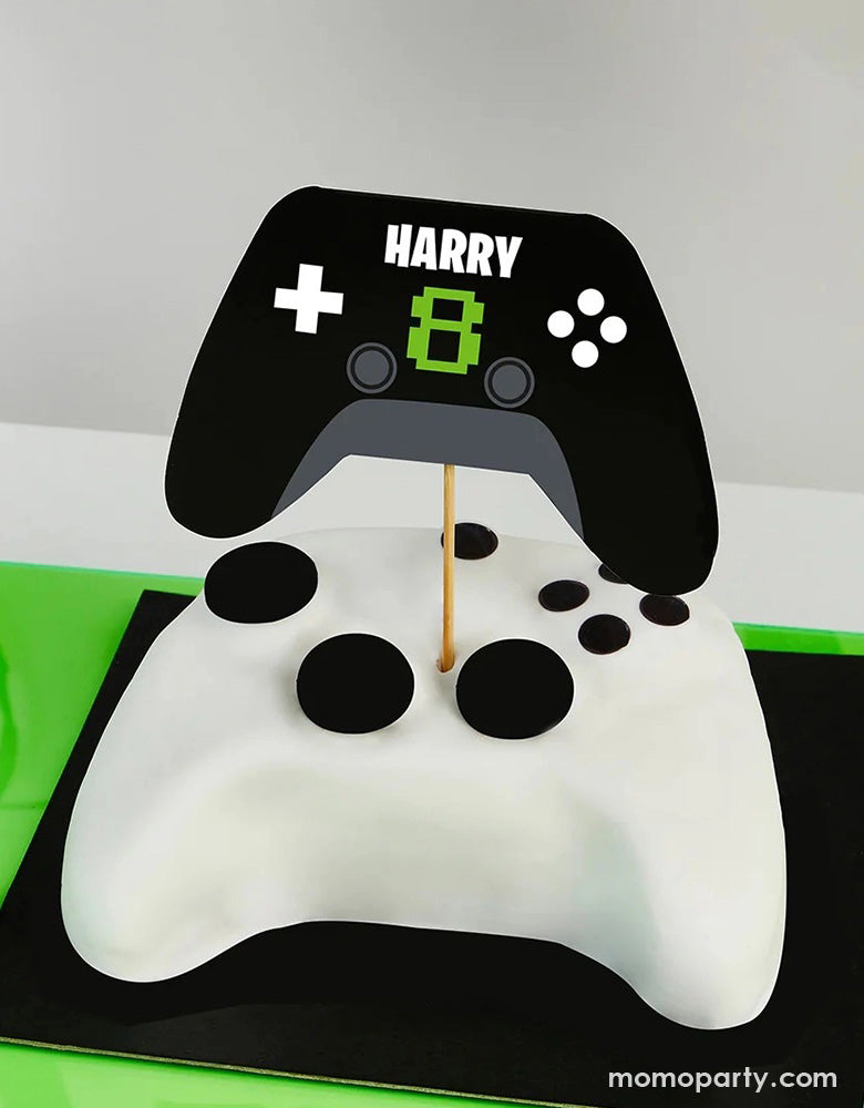 A video game console controller shaped fondant cake topped with Momo Party's Video Game Console Controller shaped personalized Cake Topper by Hooty Balloo. Come with two sticker sheets, you can customize this cake topper with the birthday person's name and age. In a classic black and green colors, it's perfect for kid's video game themed birthday party.